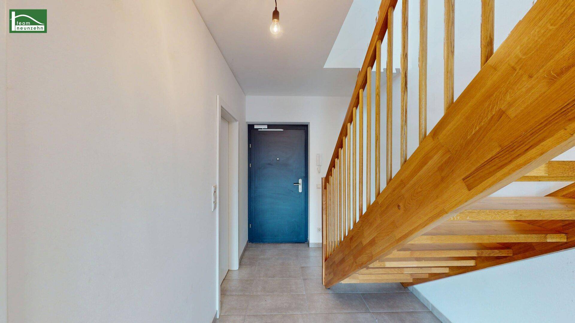 Eingangsbereich mit Fliesenboden, Holztreppe und einer modernen Eingangstür.