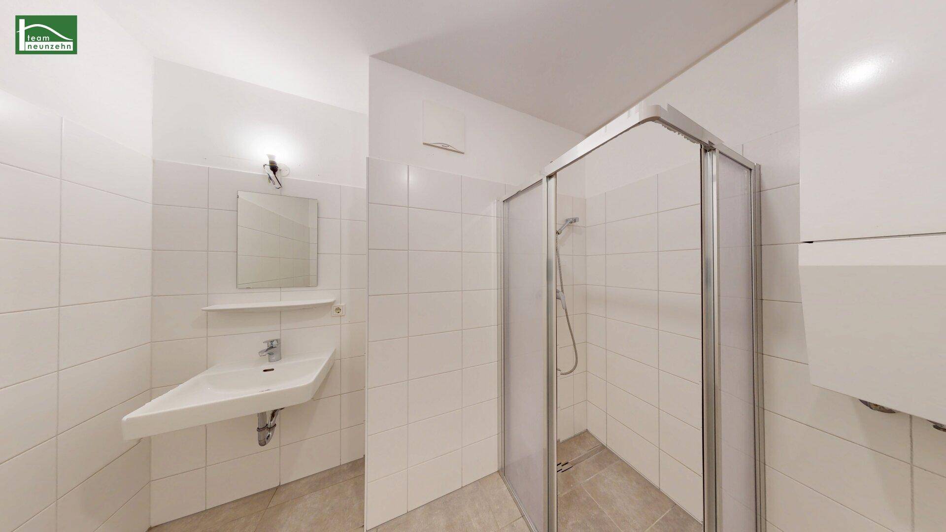 Funktionales Badezimmer mit weißen Fliesen, Waschbecken und einer Duschkabine.