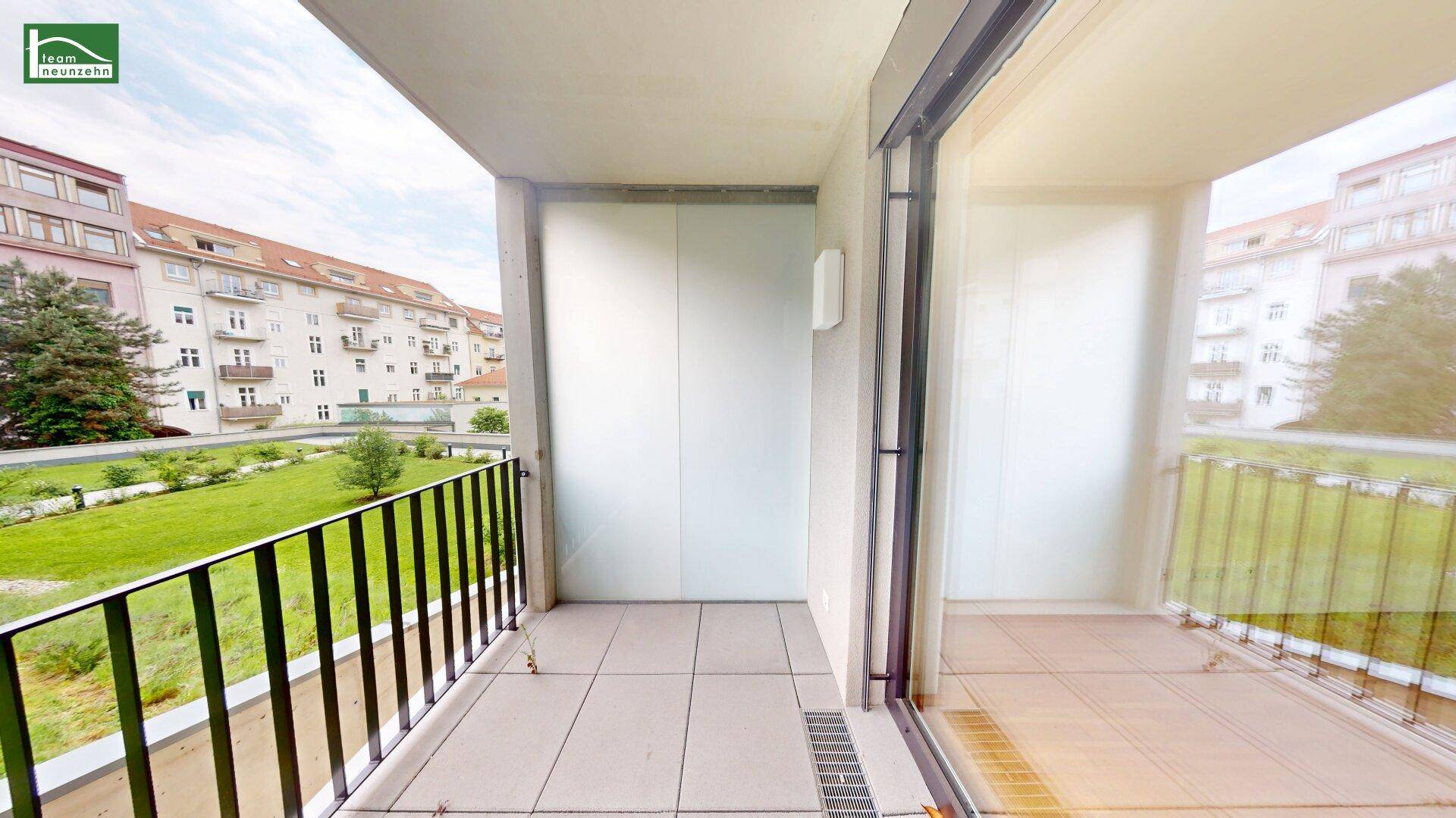 Balkon mit Fliesenboden und Blick auf eine Grünfläche sowie umliegende Gebäude.
