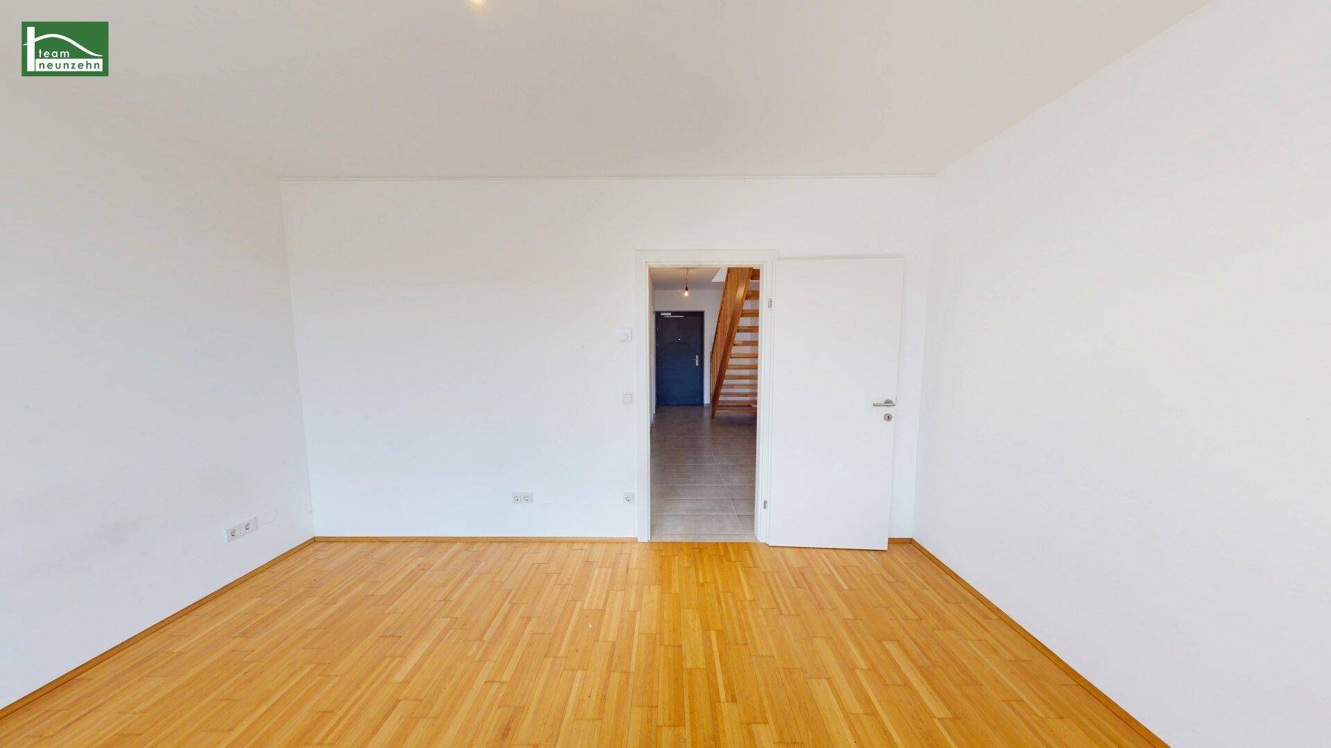 Geräumiges Zimmer mit Holzboden und Zugang zu einem Flur mit Holztreppe.