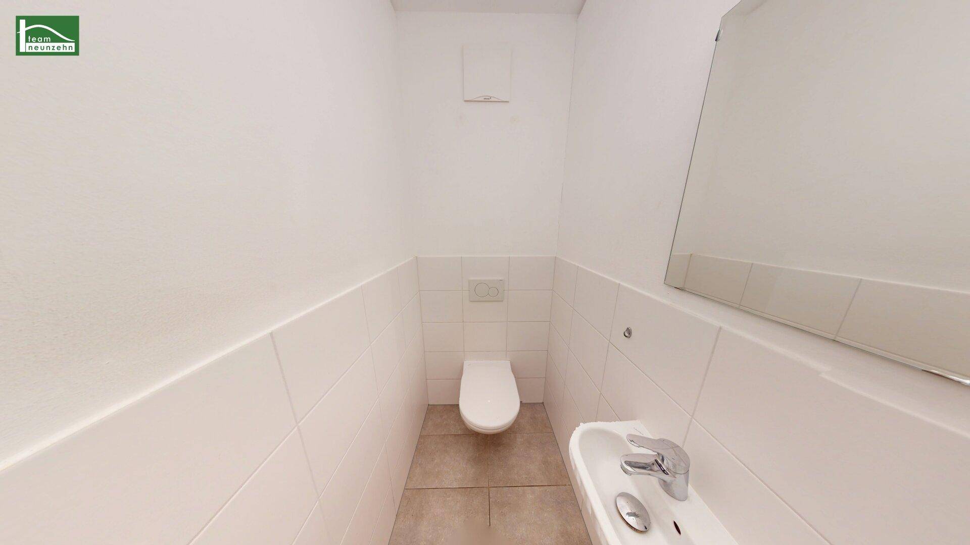 Kleines Gäste-WC mit weißer Toilette und Waschbecken, halbhoch gefliest.