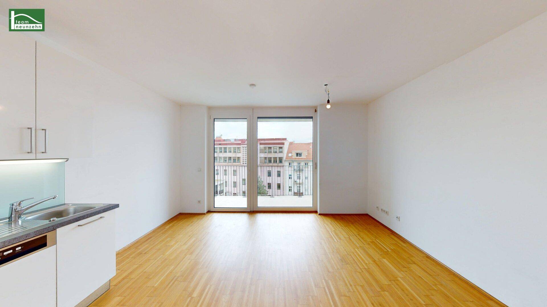 Heller Wohnbereich mit großen Fenstern, Holzboden und Zugang zu einem französischen Balkon.