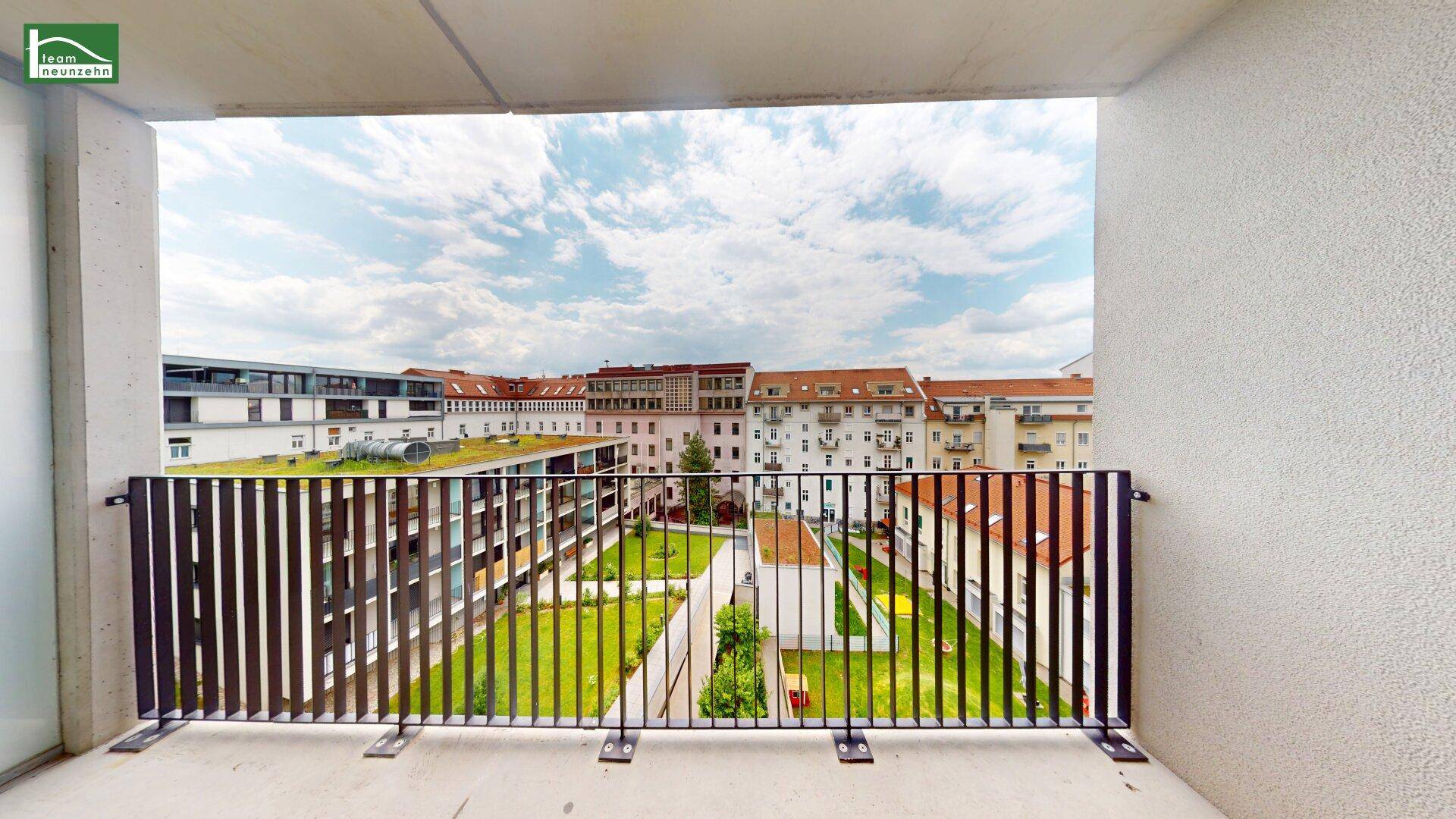 Breiter Balkon mit Metallgeländer und weitem Blick über die Stadt und grüne Innenhöfe.