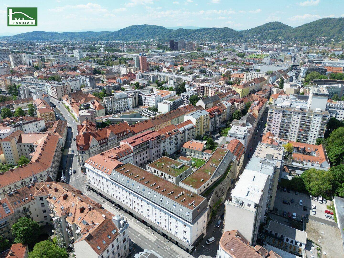 Luftaufnahme einer Stadt mit Wohngebäuden und Bergen im Hintergrund unter blauem Himmel.