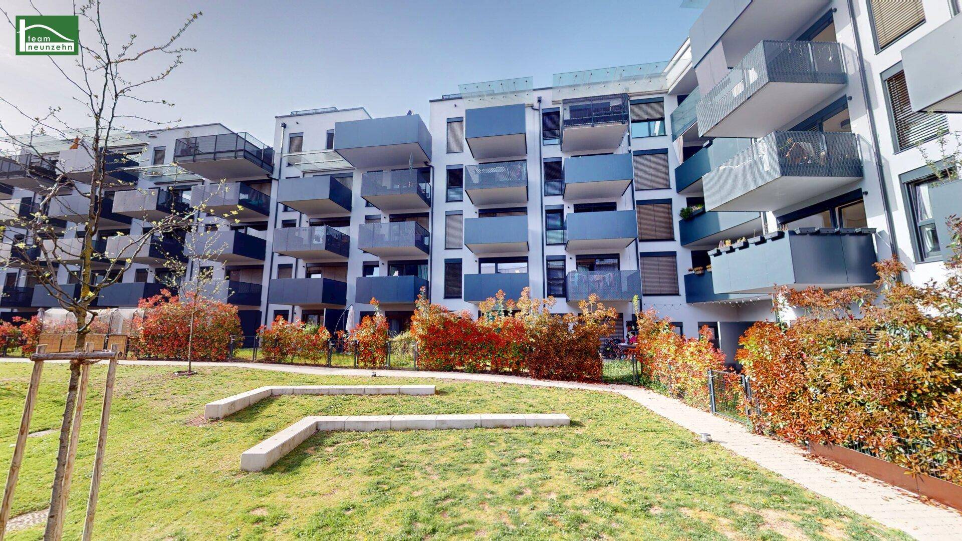 Moderne Wohngebäude mit zahlreichen Balkonen und einem begrünten Innenhof unter blauem Himmel.