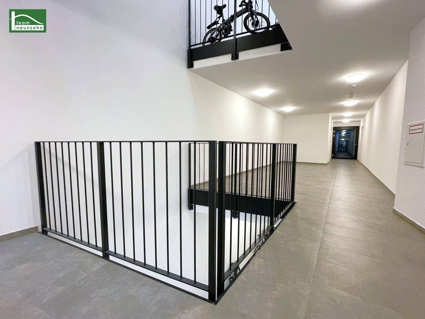 Langer, heller Flur mit Fliesenboden und modernem Geländer, ein Fahrrad ist sichtbar.