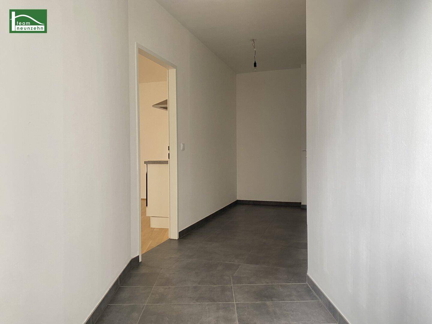 Heller Flur mit dunklen Bodenfliesen und weiß gestrichenen Wänden, der zu weiteren Räumen führt.