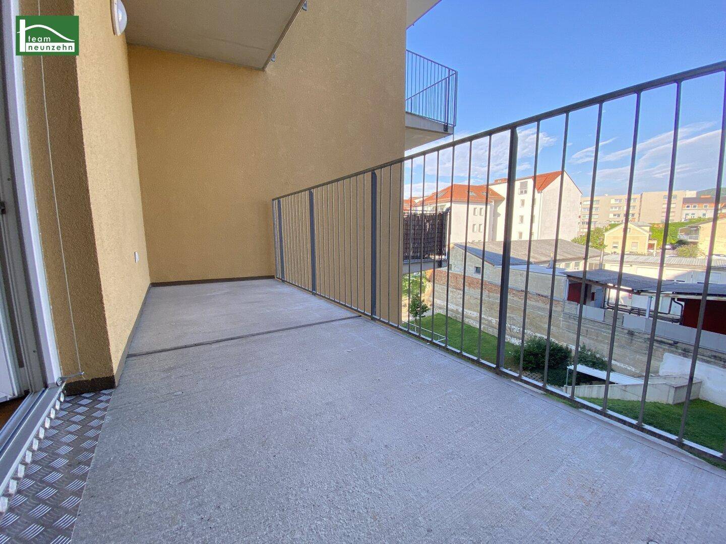 Geräumiger Balkon mit Metallgeländer und Blick auf die städtische Umgebung unter blauem Himmel.