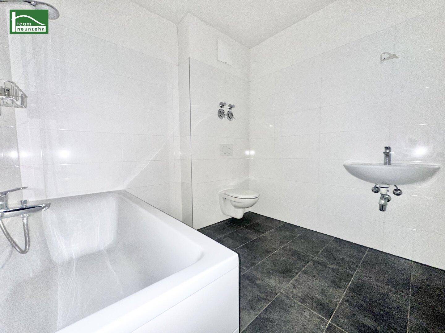 Modernes Badezimmer mit weißen Wandfliesen, dunklem Boden, Badewanne, wandhängendem WC und Waschbecken.