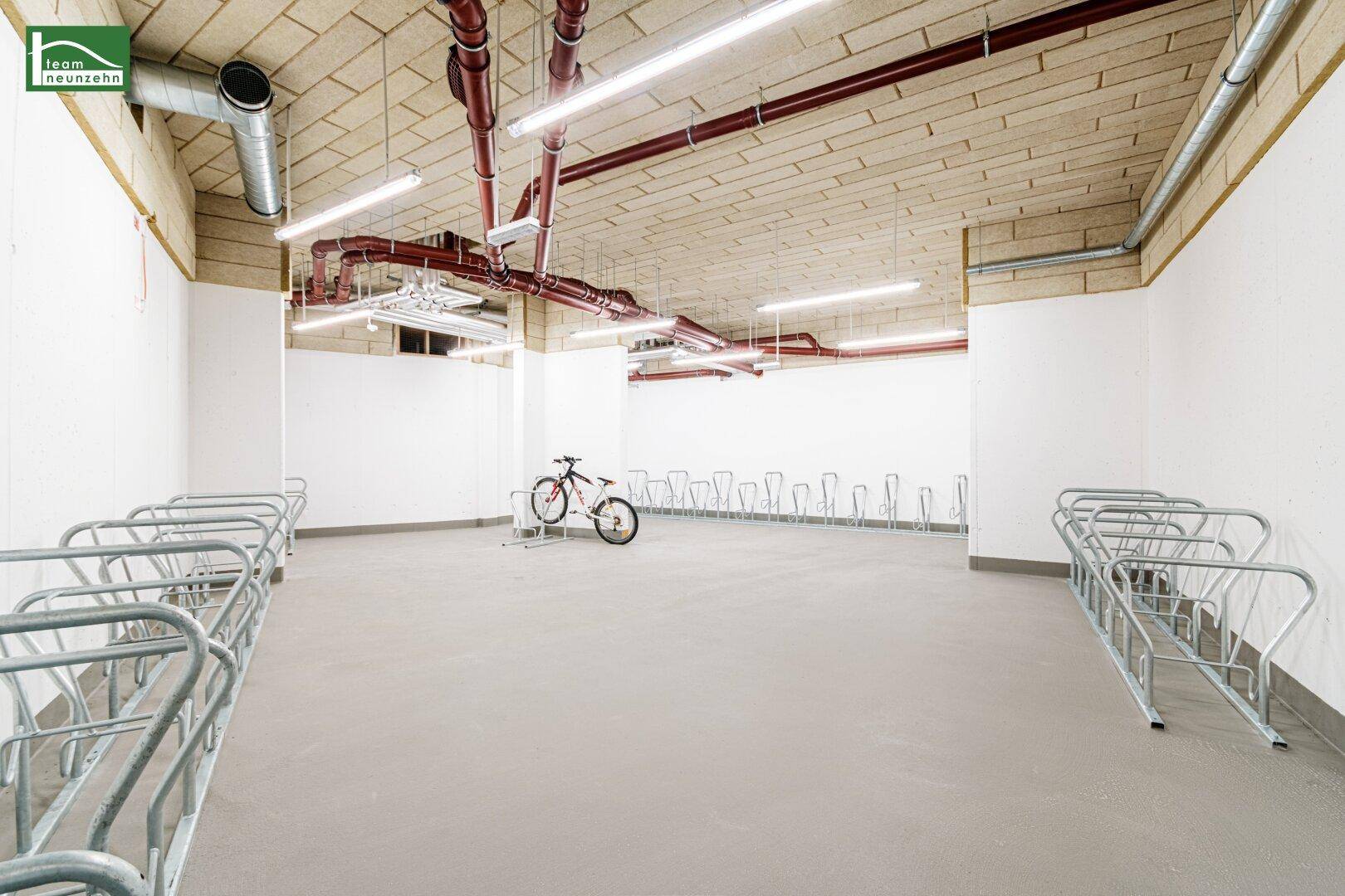 Geräumiger Fahrradraum mit zahlreichen Abstellmöglichkeiten und sichtbaren Installationen an der Decke.