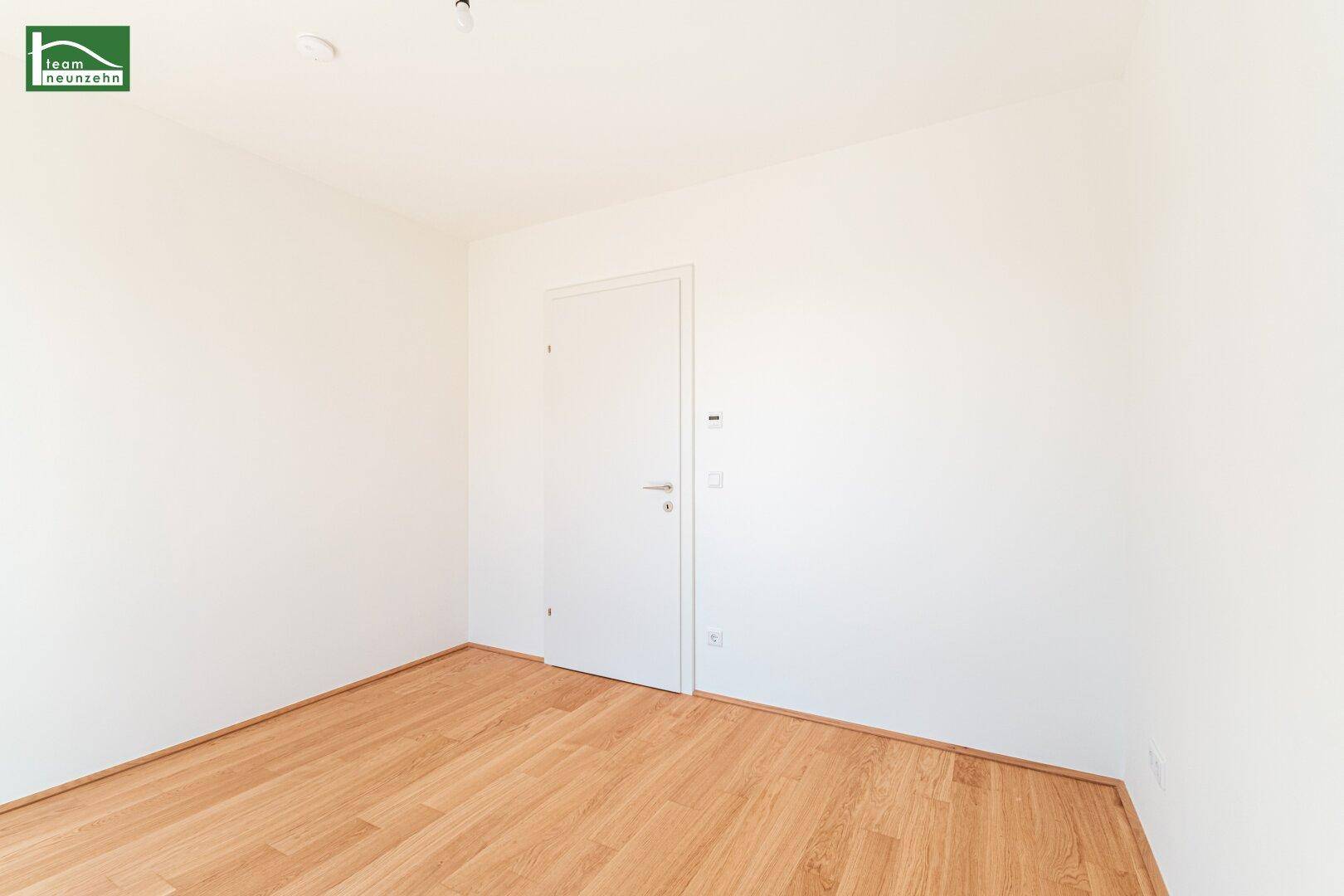 Leeres Zimmer mit Holzboden und weißer Tür, bietet eine neutrale Basis für Einrichtung.