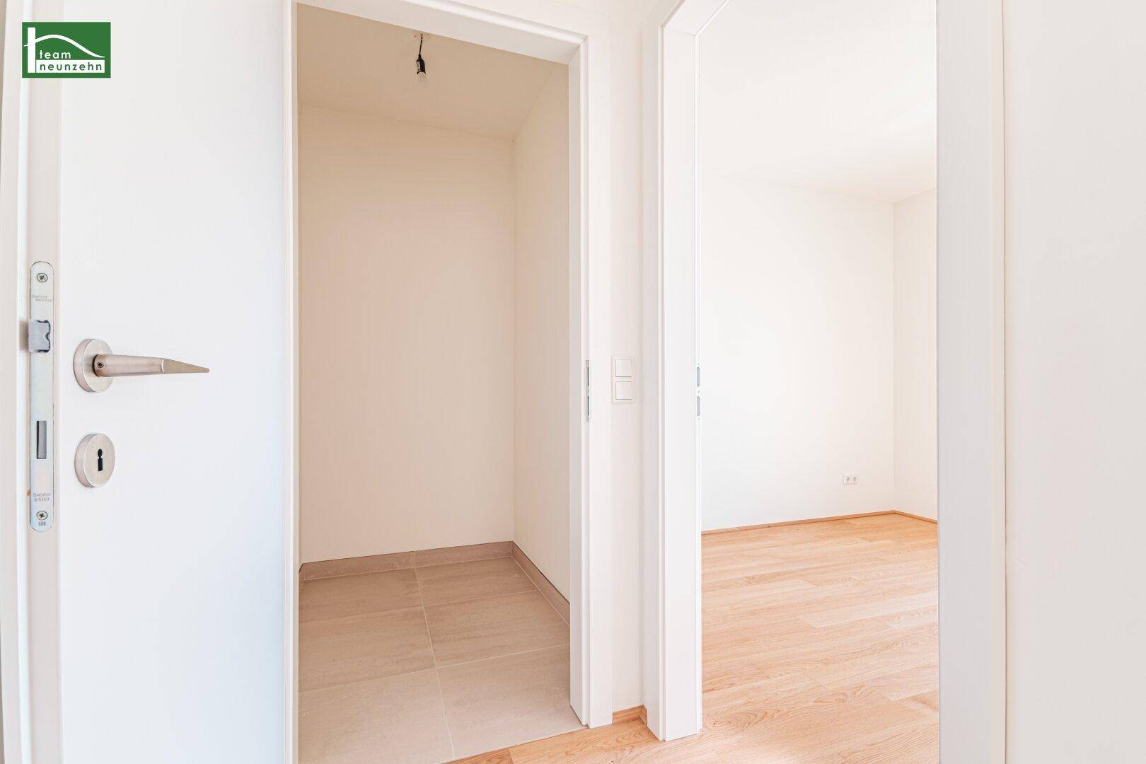 Flur mit Blick in eine kleine Abstellnische mit Fliesenboden und angrenzendem Zimmer.