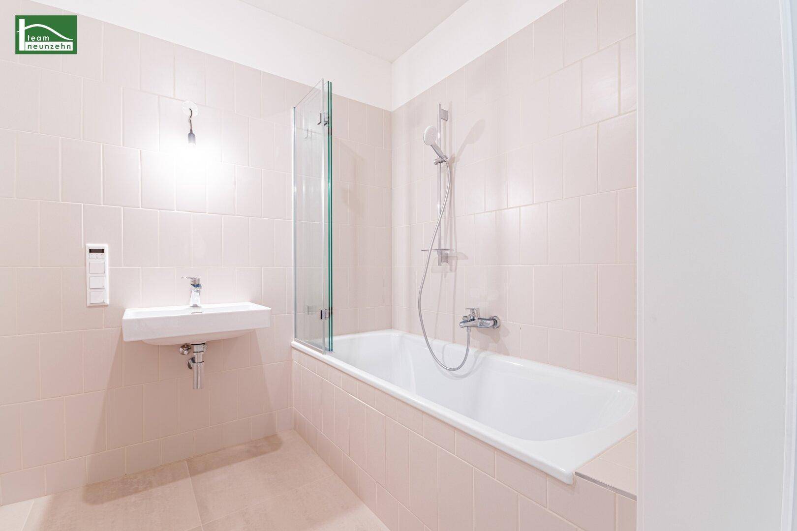 Modernes Badezimmer mit Badewanne, Duschwand und Einzelwaschbecken, in hellen Rosatönen gefliest.