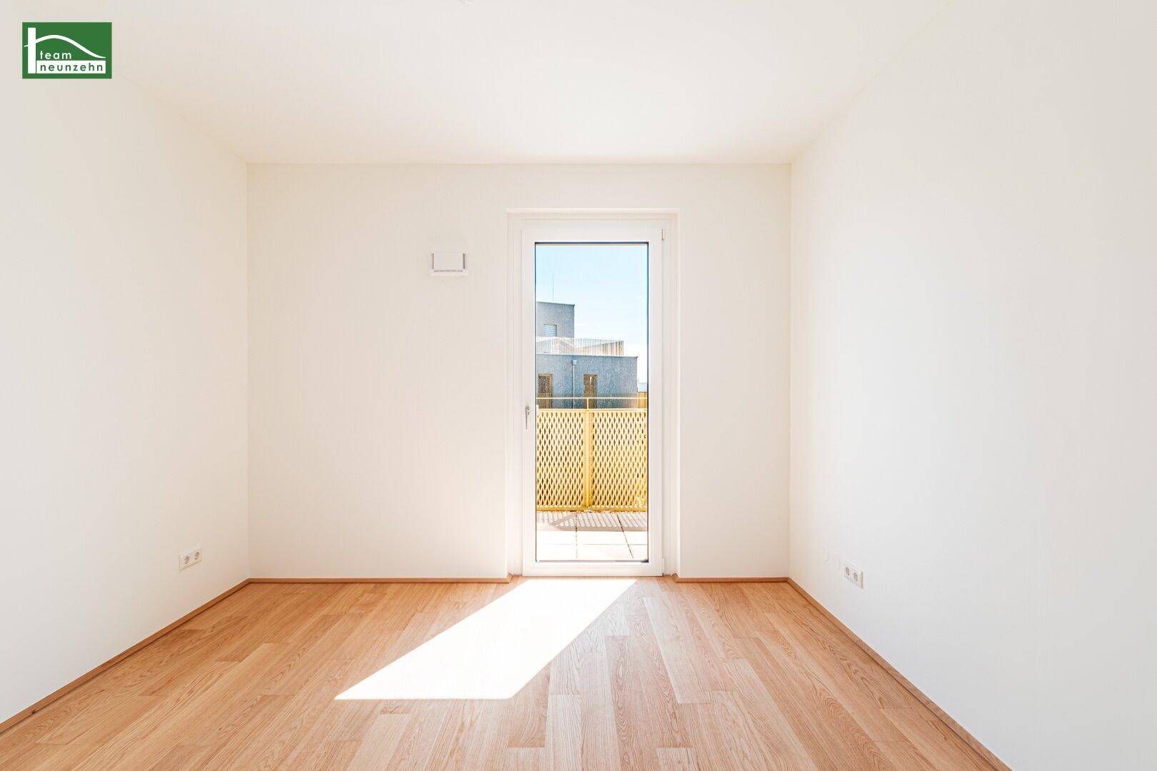 Helles, leeres Zimmer mit Holzboden und Zugang zu einem Balkon, ideal als Schlafzimmer.