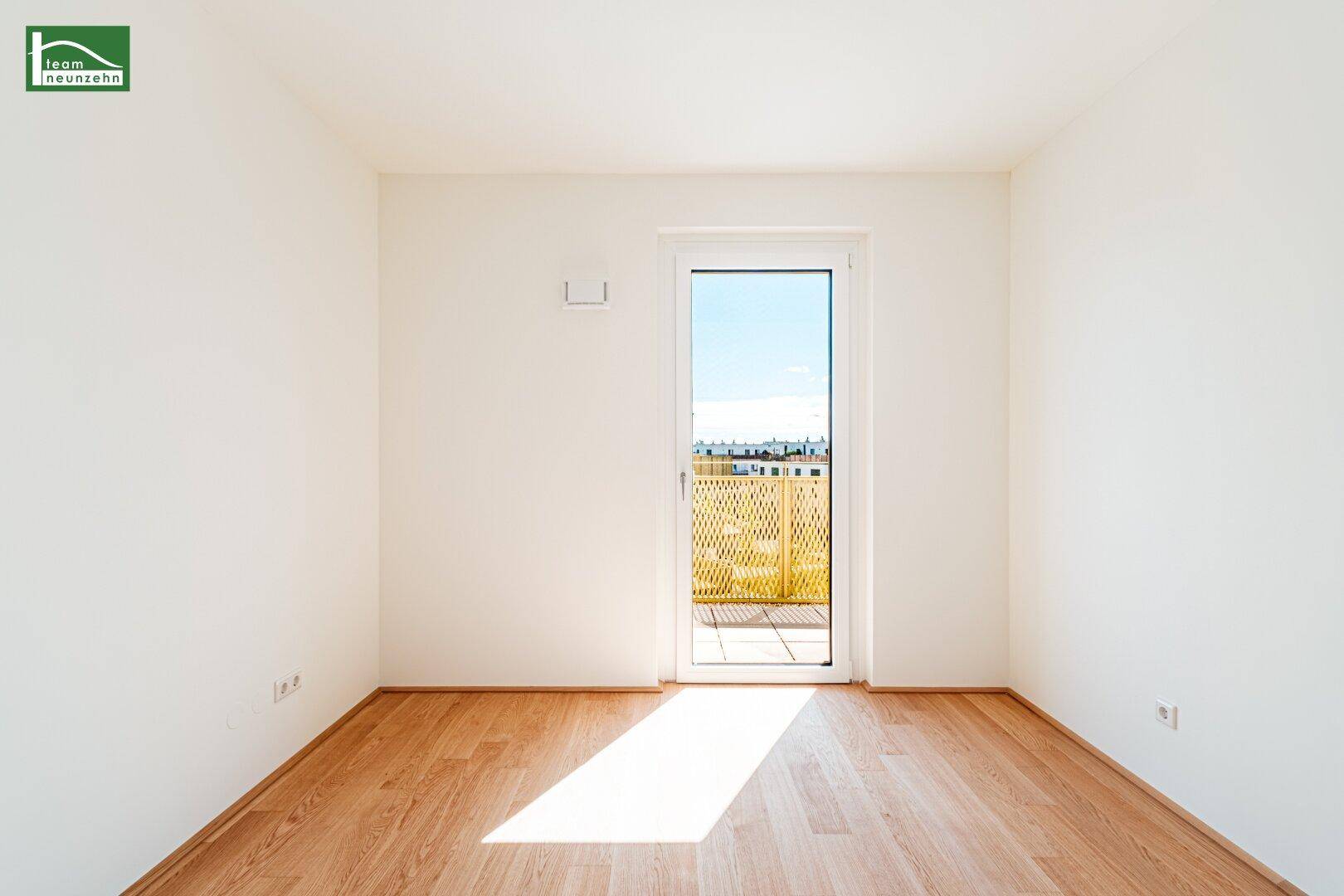 Helles Zimmer mit Holzboden und einer Fenstertür, die auf einen Balkon führt.