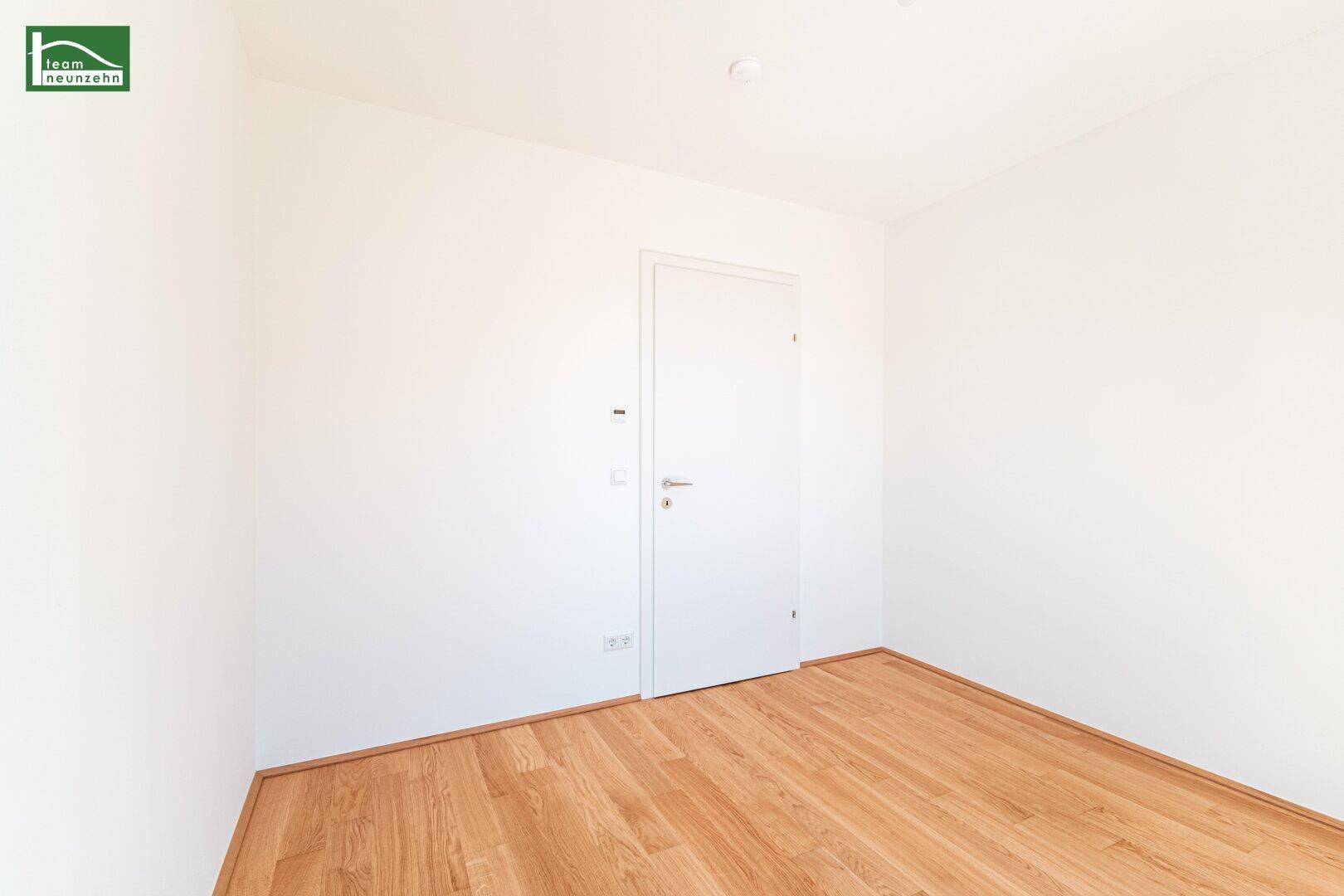 Leeres Zimmer mit hellem Holzboden und weißer Tür, ideal für ein Schlaf- oder Arbeitszimmer.