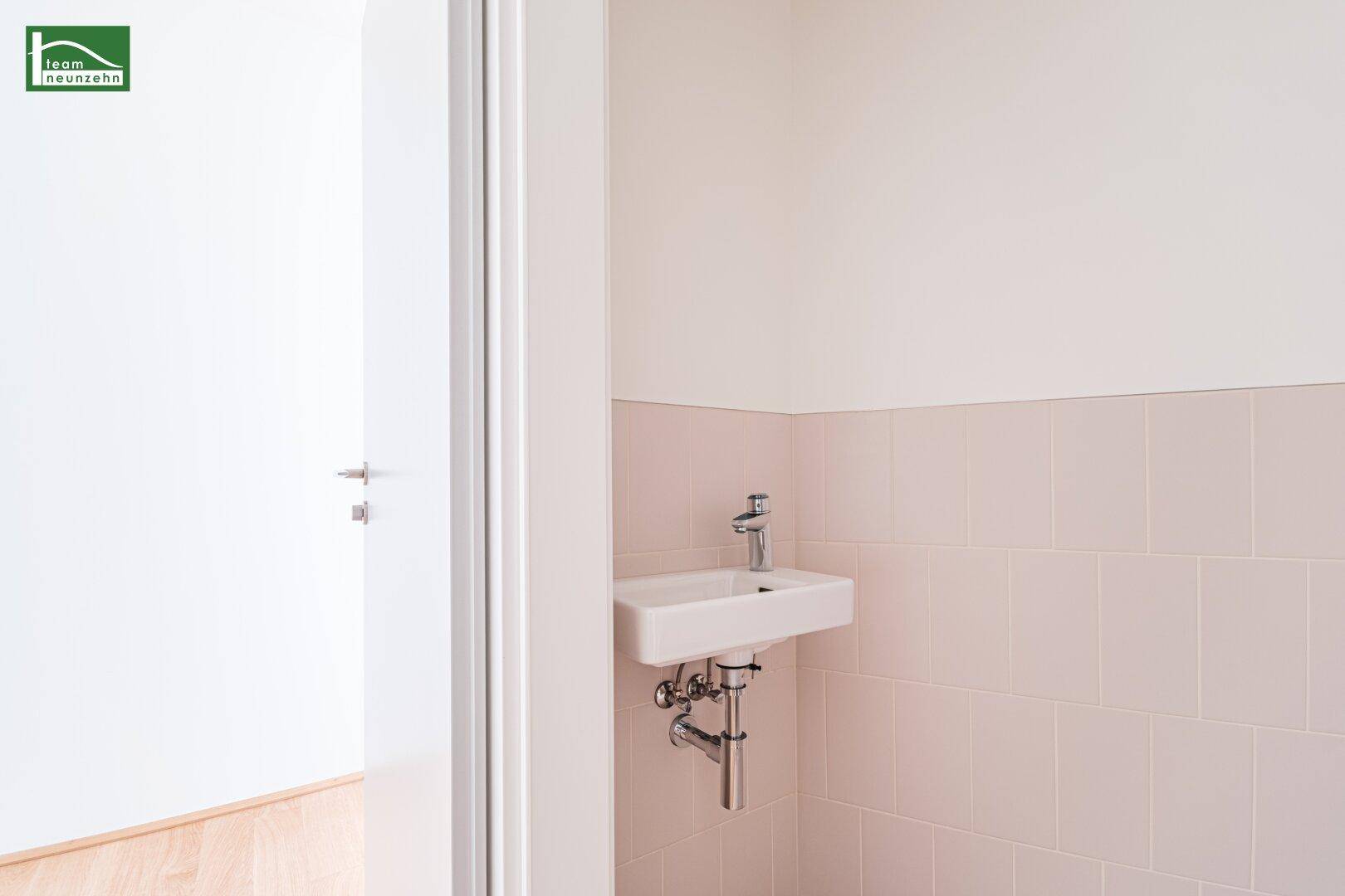 Kleines Waschbecken in einem separaten WC mit hellen Fliesen und weißer Wand.