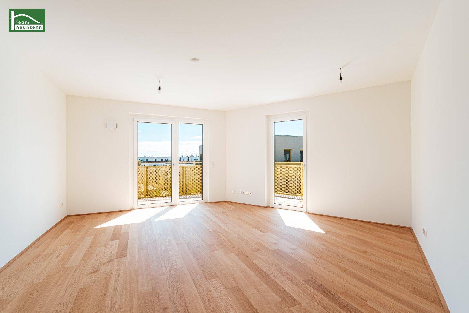 Lichtdurchfluteter Wohnraum mit zwei großen Fenstertüren und hellem Parkettboden.