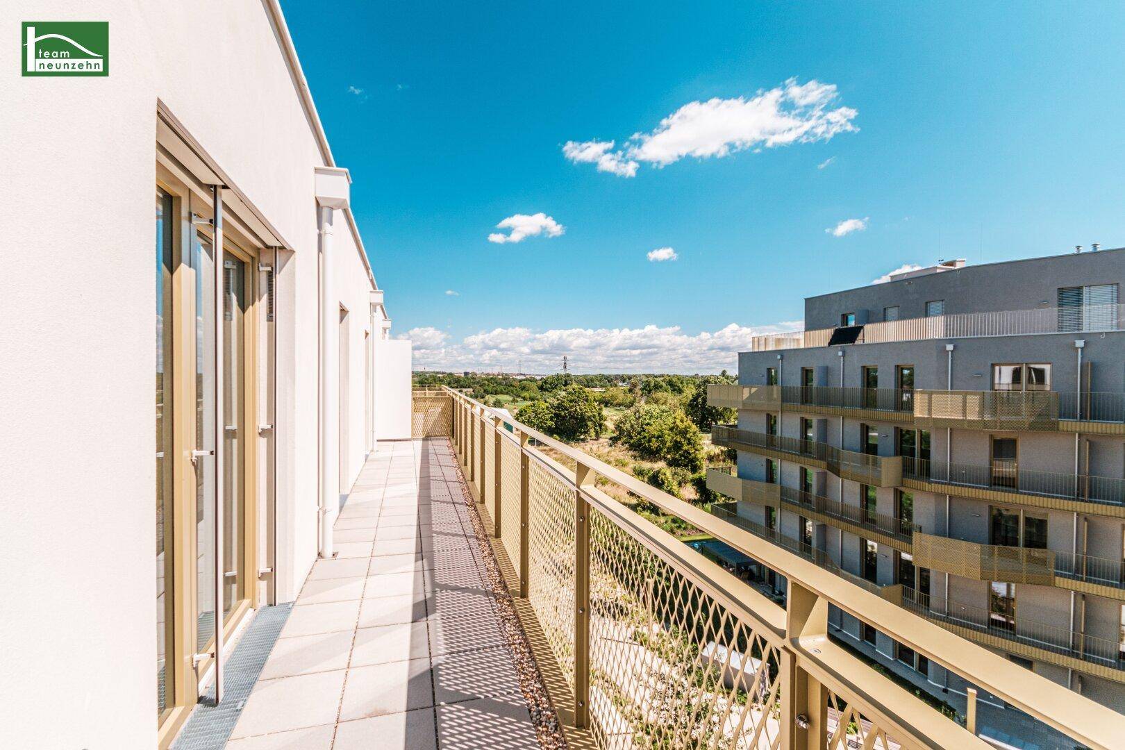 Sonniger Balkon mit weitem Blick ins Grüne und auf weitere Gebäude.