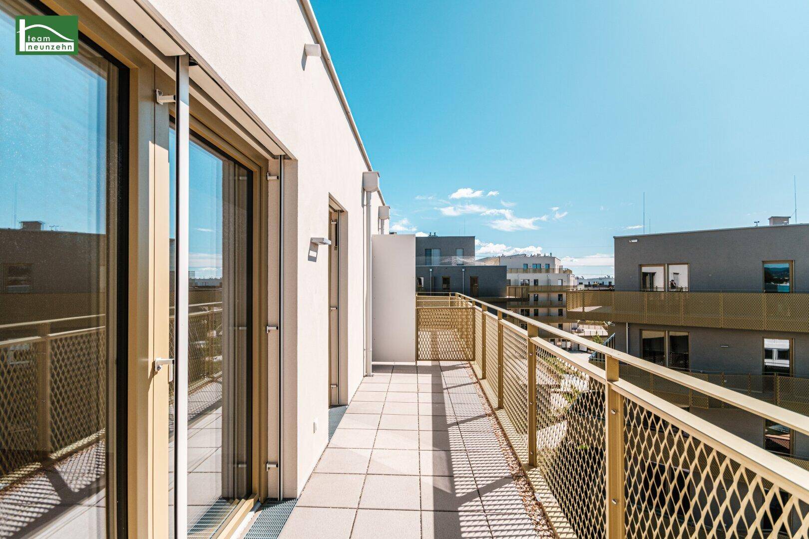 Heller Balkon mit Fliesenboden und goldenem Geländer, zugänglich durch große Glasschiebetüren.