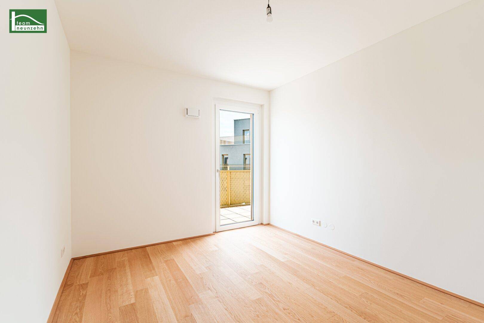 Heller, leerer Raum mit weißen Wänden und hellem Holzfußboden, mit Zugang zu einem Balkon.