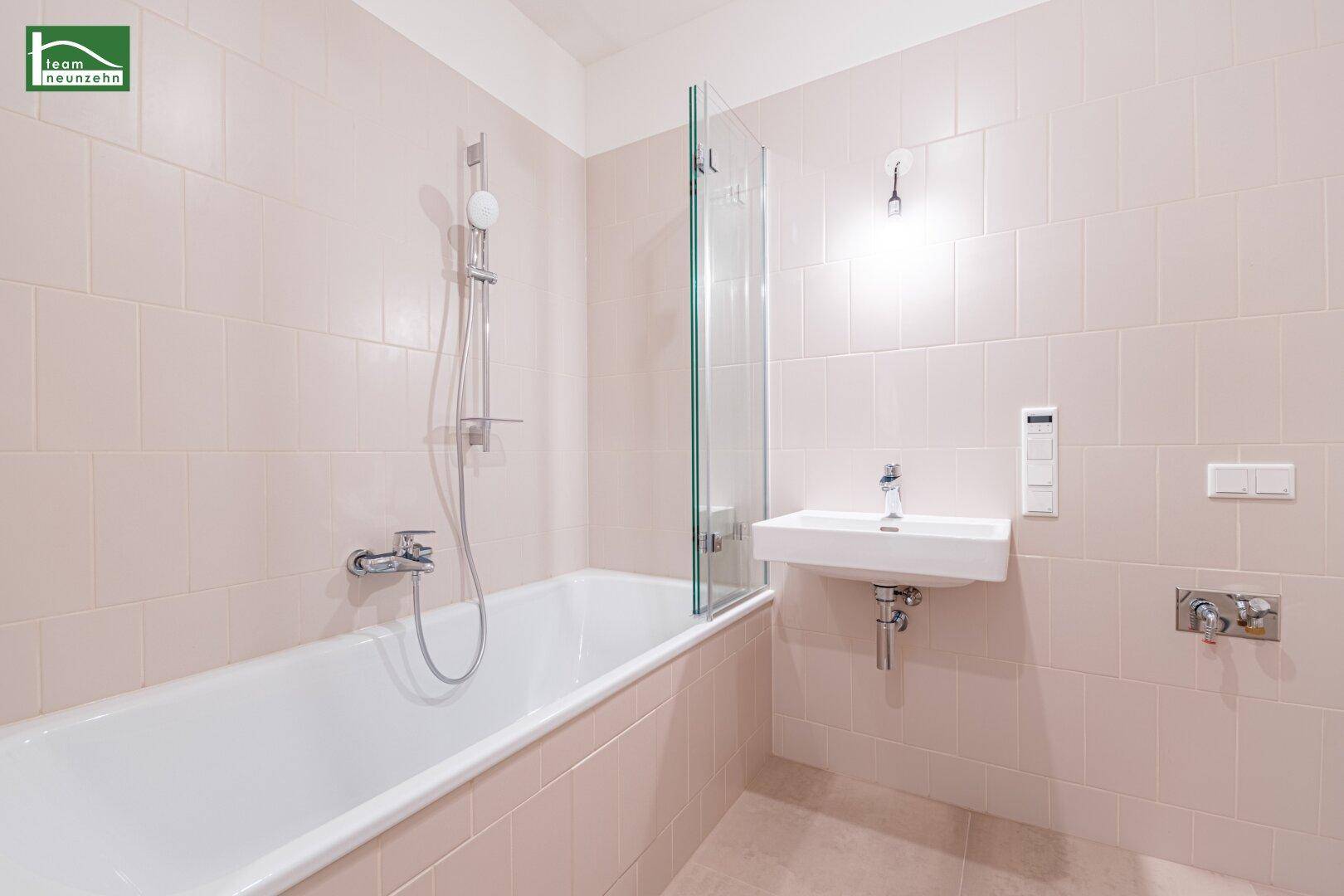Modernes Badezimmer mit hellbeigen Fliesen, Badewanne mit Duschwand und einem einzelnen Waschbecken.
