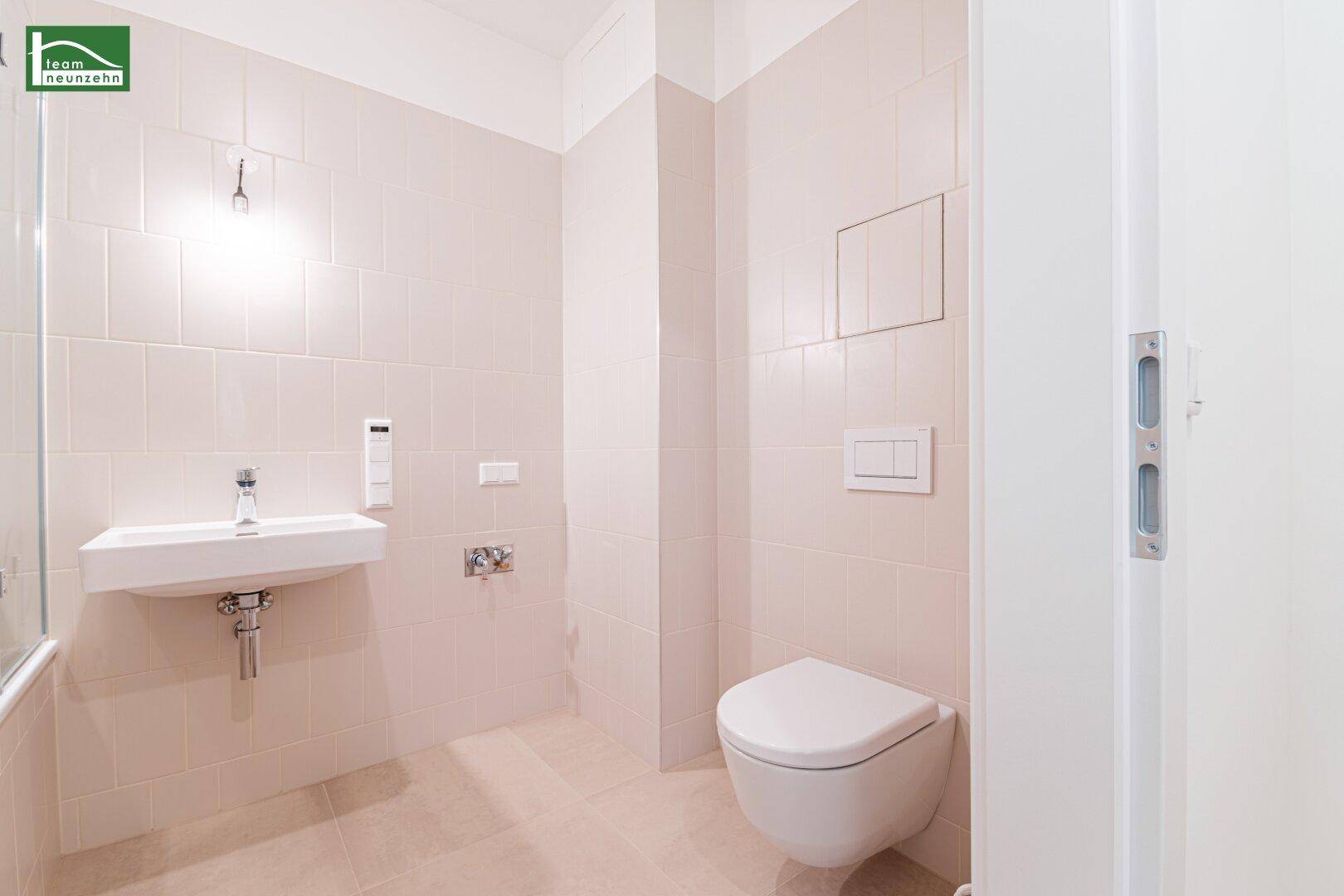 Modernes Badezimmer mit wandhängendem WC und Waschbecken, komplett gefliest in hellen Tönen.