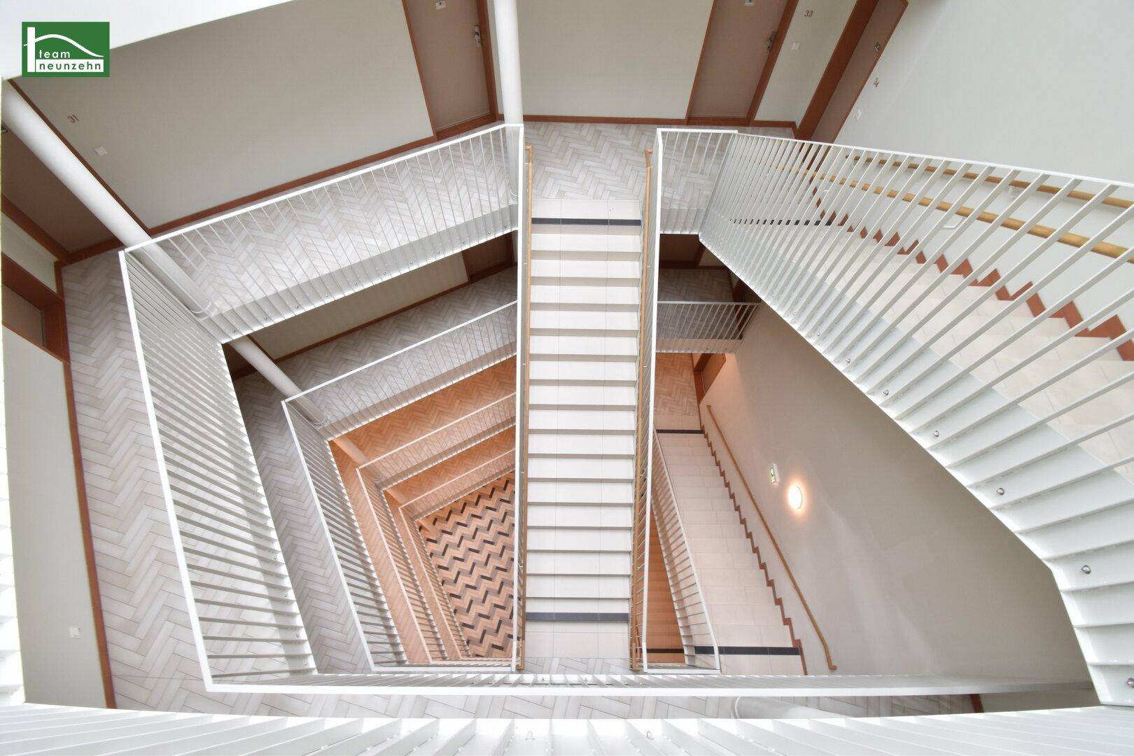 Blick von oben auf ein modernes Treppenhaus mit mehreren Etagen und gemusterten Fliesenböden.