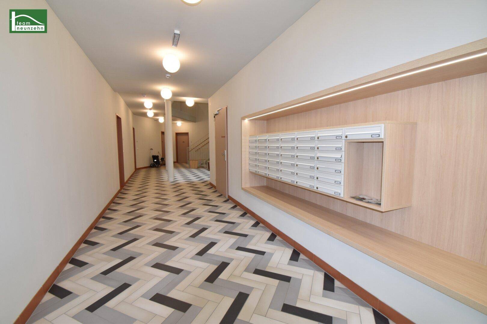 Langer Flur mit integrierten Briefkästen, modernen Deckenleuchten und gemustertem Fliesenboden.
