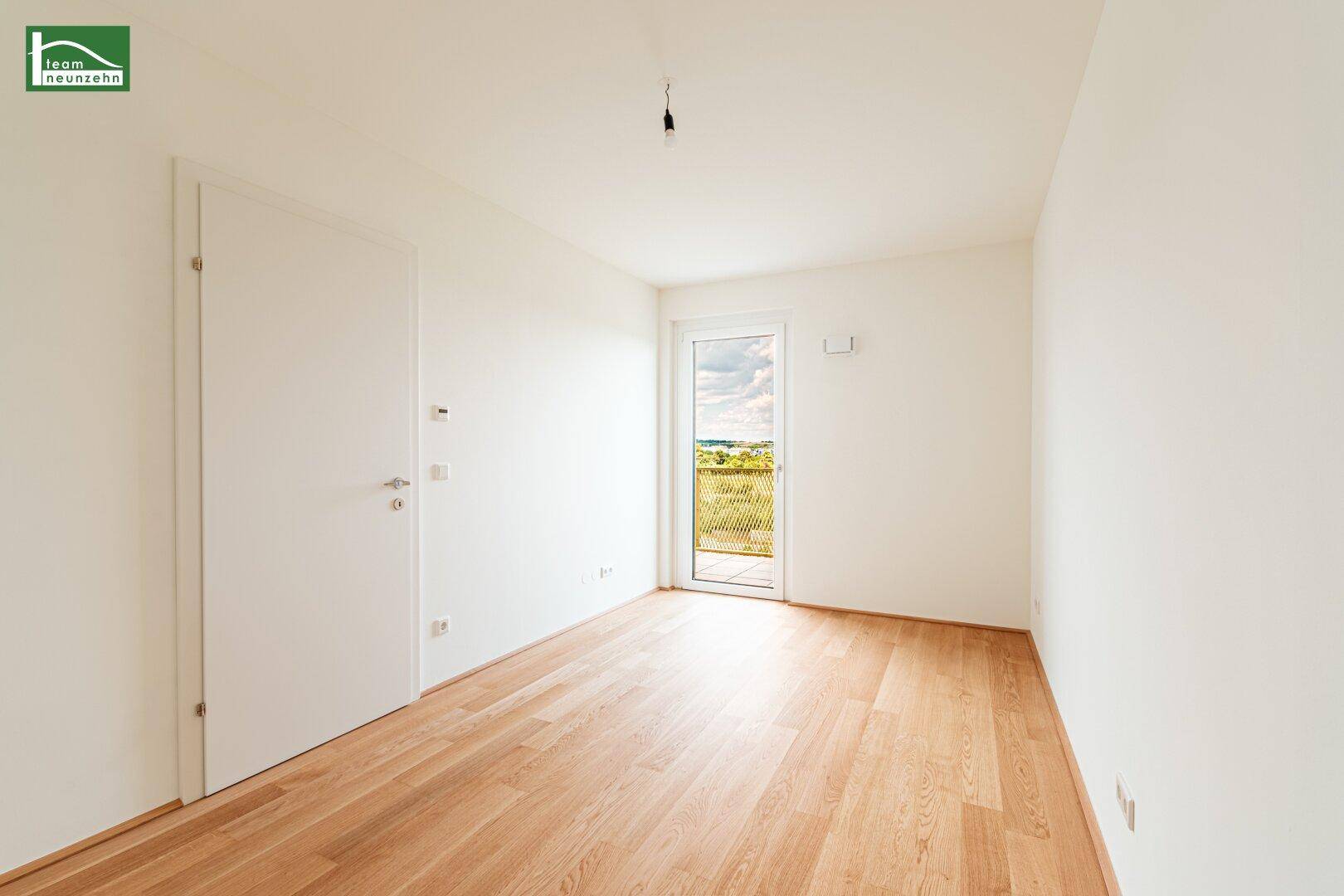 Leeres Zimmer mit Holzboden und Fenster, das viel Tageslicht hereinlässt.