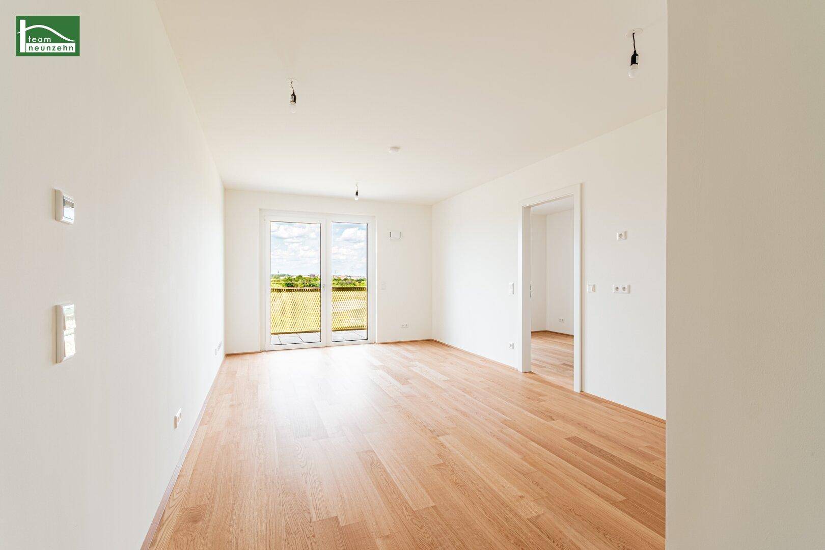 Helles, leeres Wohnzimmer mit Holzboden und Zugang zu einem Balkon.