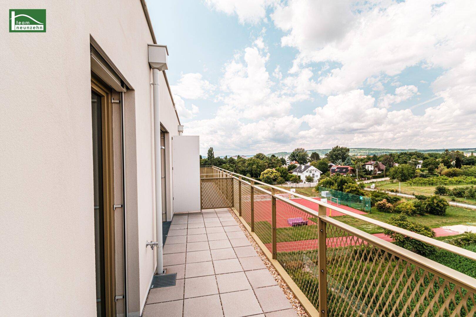 Langer Balkon mit Fliesenboden und Metallgeländer, bietet weite Aussicht auf die Umgebung.