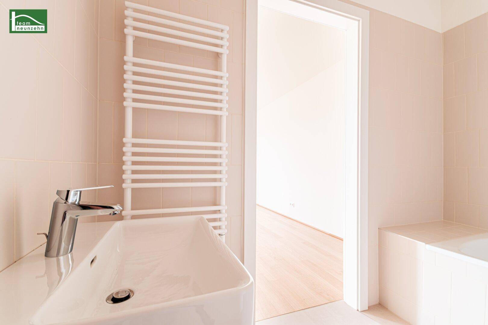 Badezimmer mit modernem Waschbecken, beheiztem Handtuchhalter und hellen Fliesen.
