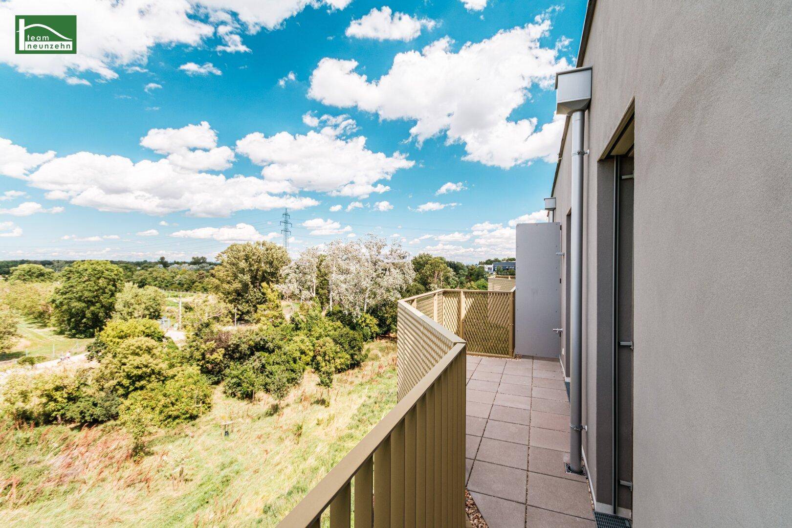 Geräumiger Balkon mit Fliesenboden und weitem Blick ins Grüne unter blauem Himmel.