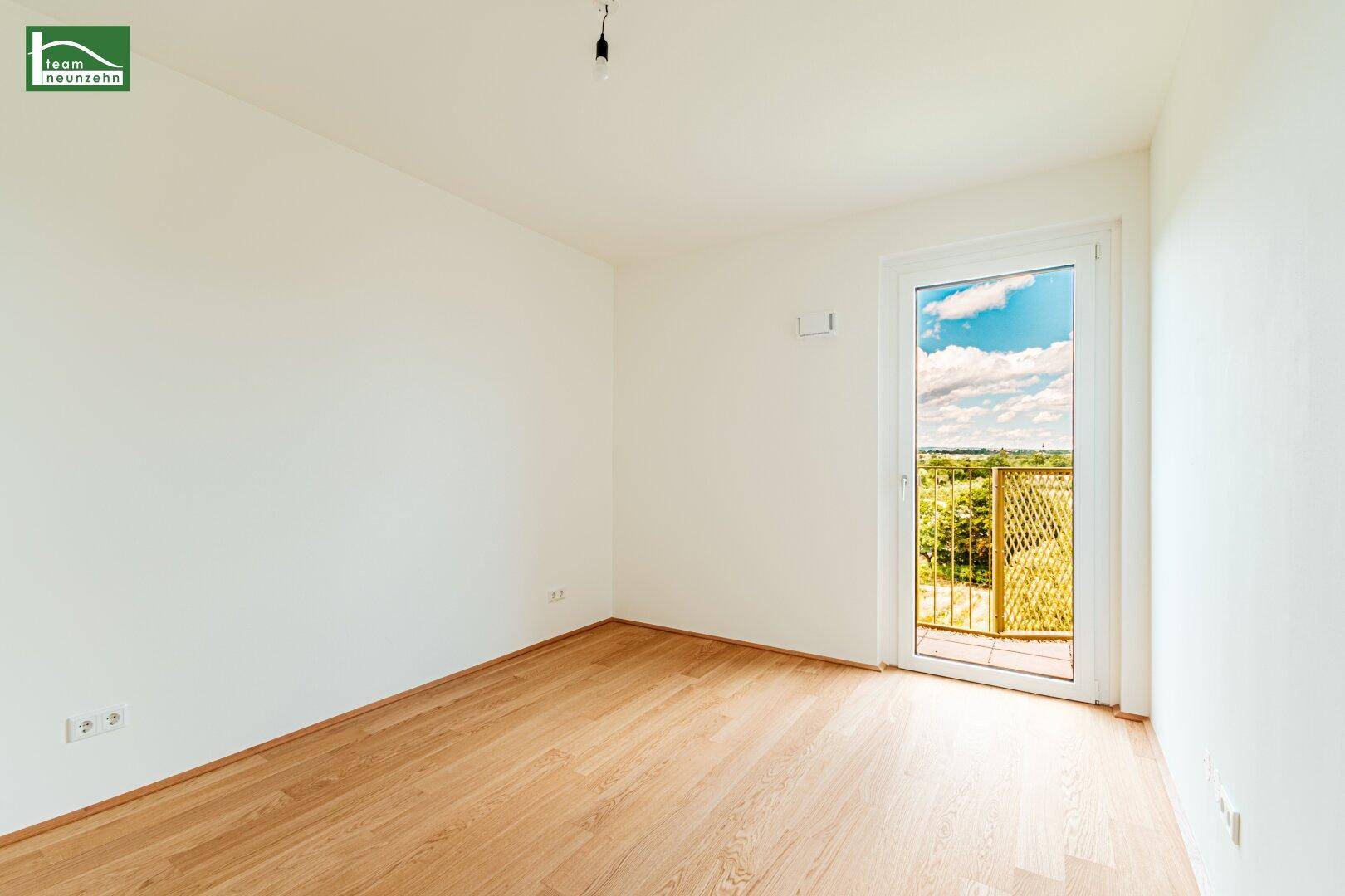 Helles, leeres Zimmer mit Holzboden und Zugang zu einem Balkon, ideal als Schlafzimmer.