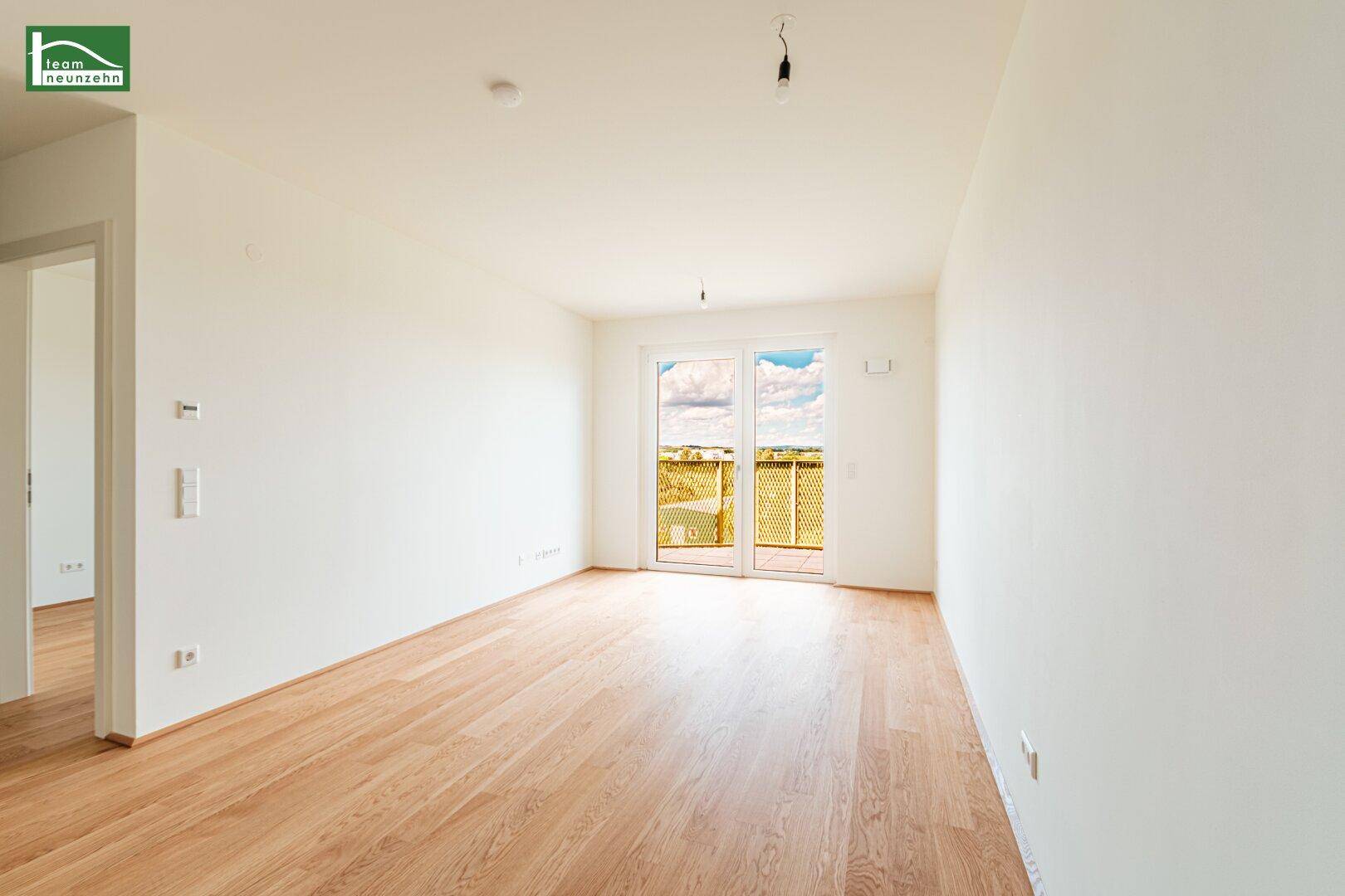 Heller Wohnbereich mit Holzboden und großen Fenstern, die Zugang zum Balkon bieten.