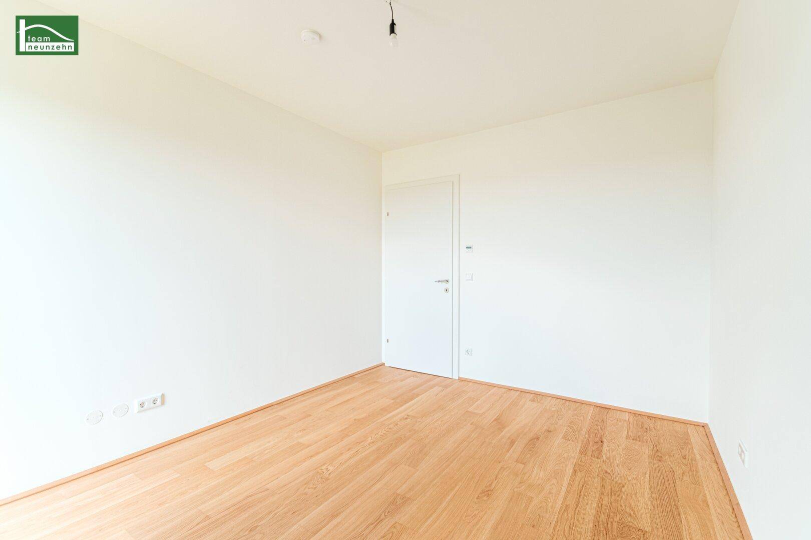 Leeres Zimmer mit hellem Holzboden und weißer Tür, bereit zur individuellen Gestaltung.