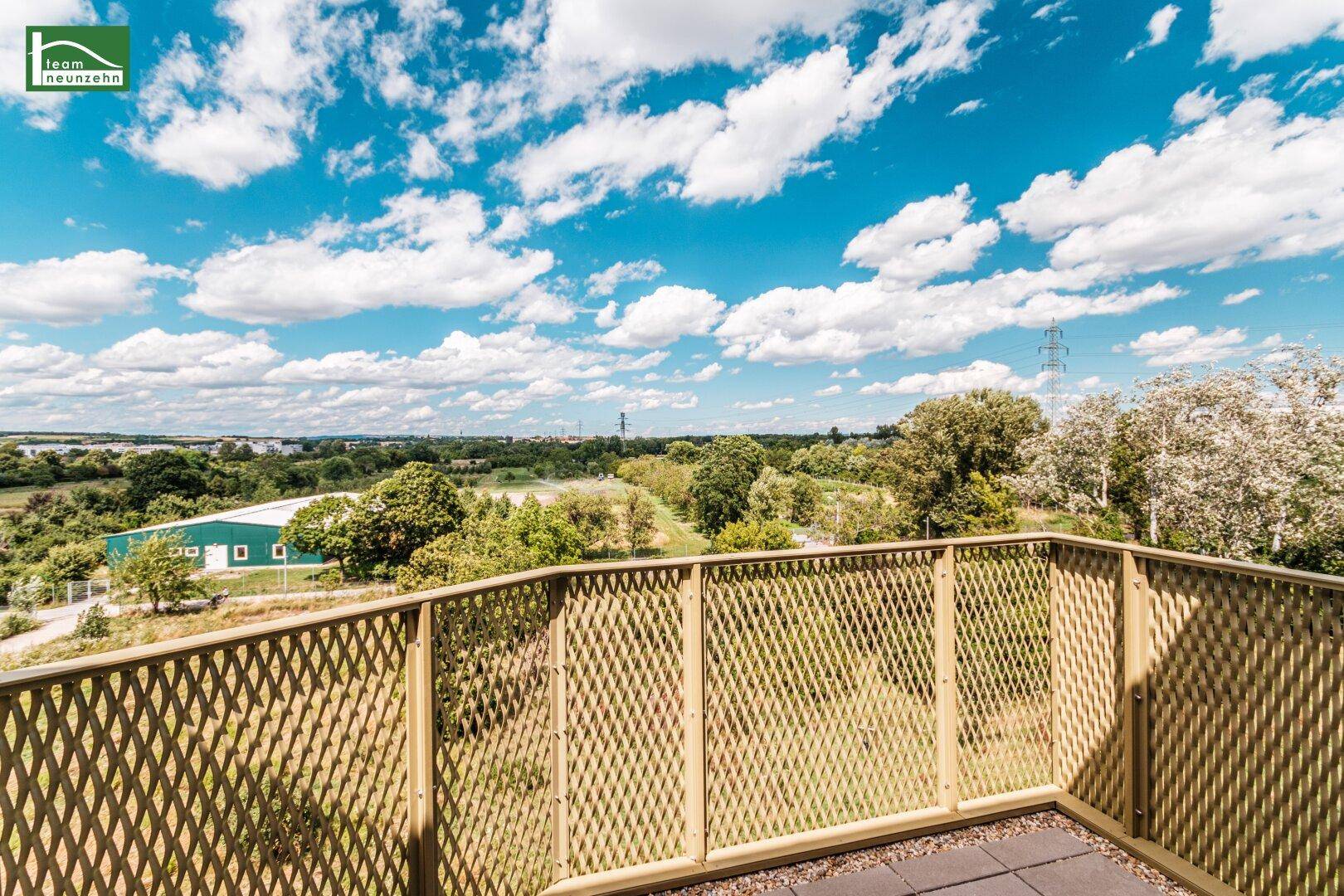 Balkon mit weitem Blick ins Grüne und über die Dächer unter strahlend blauem Himmel.