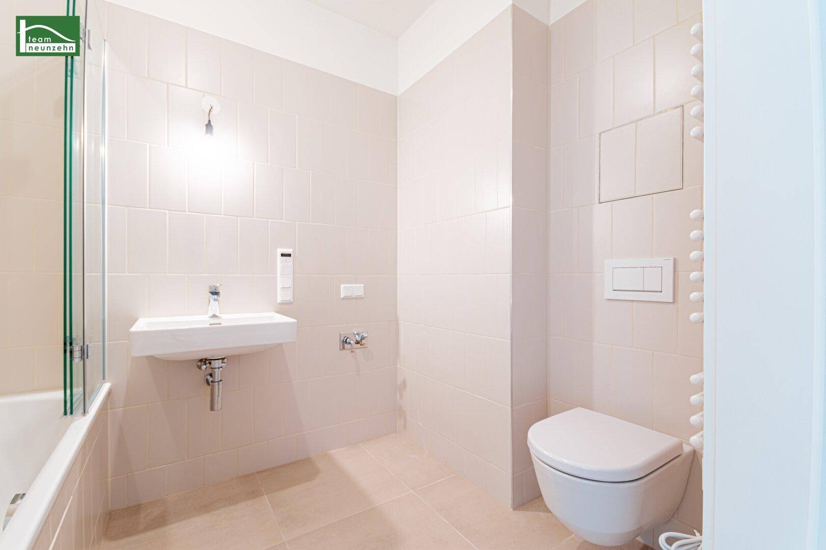 Helles Badezimmer mit Wand-WC, Waschbecken und beigefarbenen Fliesen.