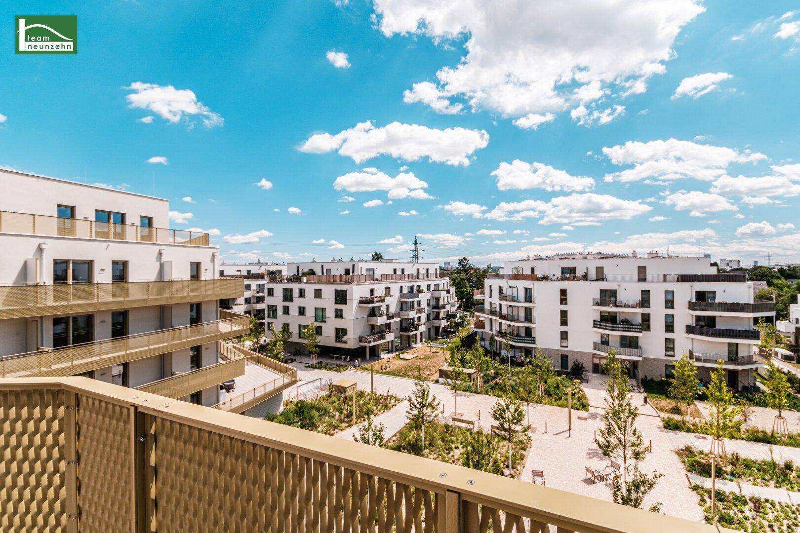 Panoramablick vom Balkon auf eine moderne Wohnanlage mit gepflegten Grünflächen und weiteren Gebäuden.