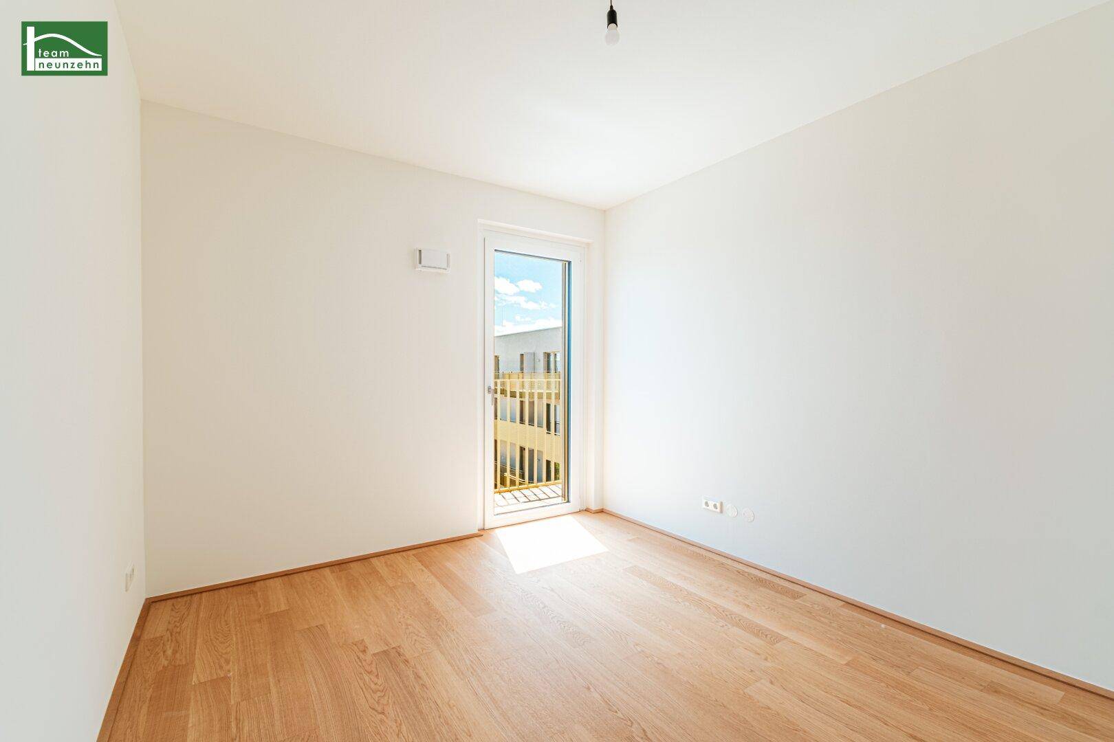 Helles, leeres Zimmer mit Holzboden und Zugang zu einem Balkon, ideal als Schlafzimmer.
