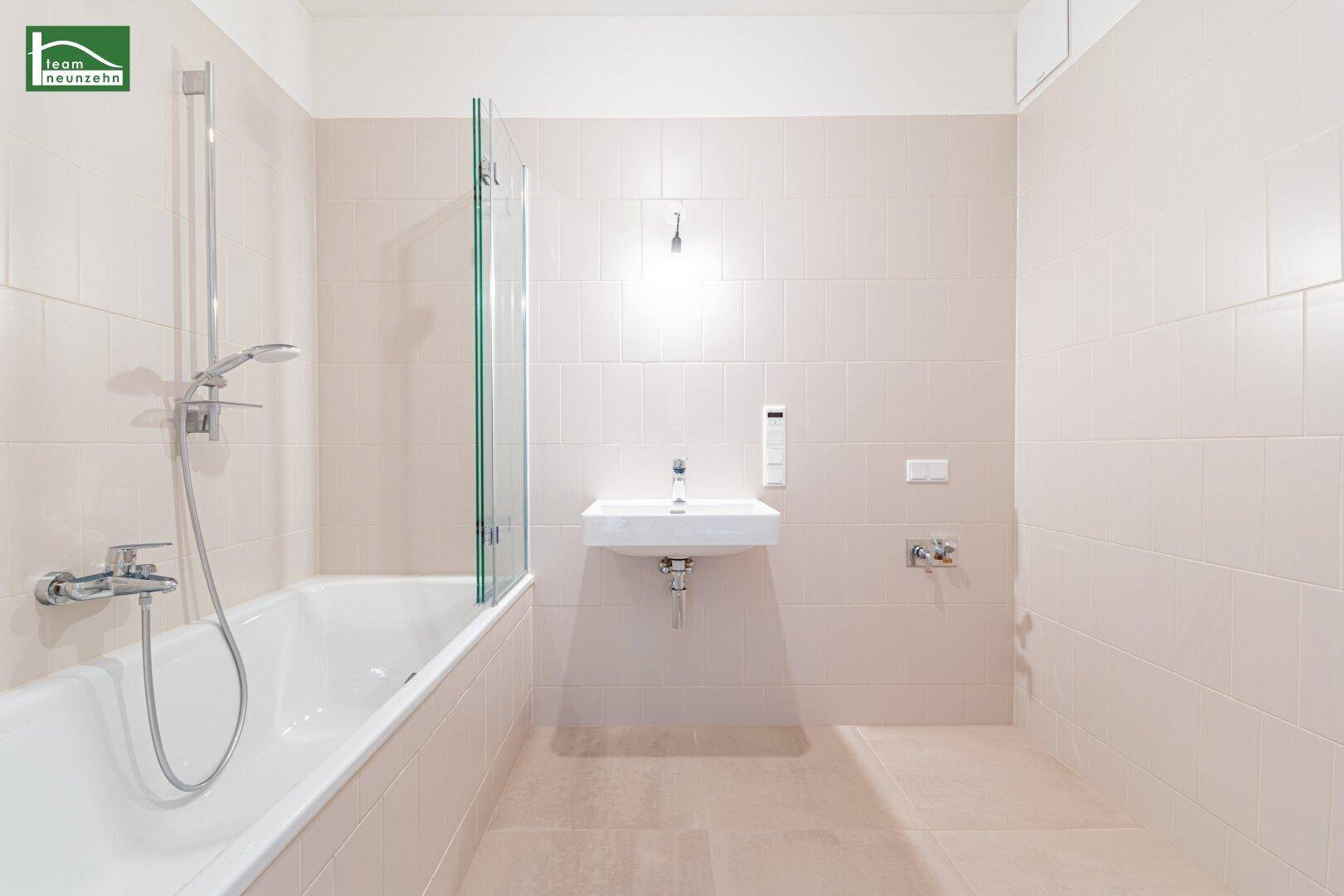 Modernes Badezimmer mit Badewanne, Duschwand und Waschbecken, hell gefliest.