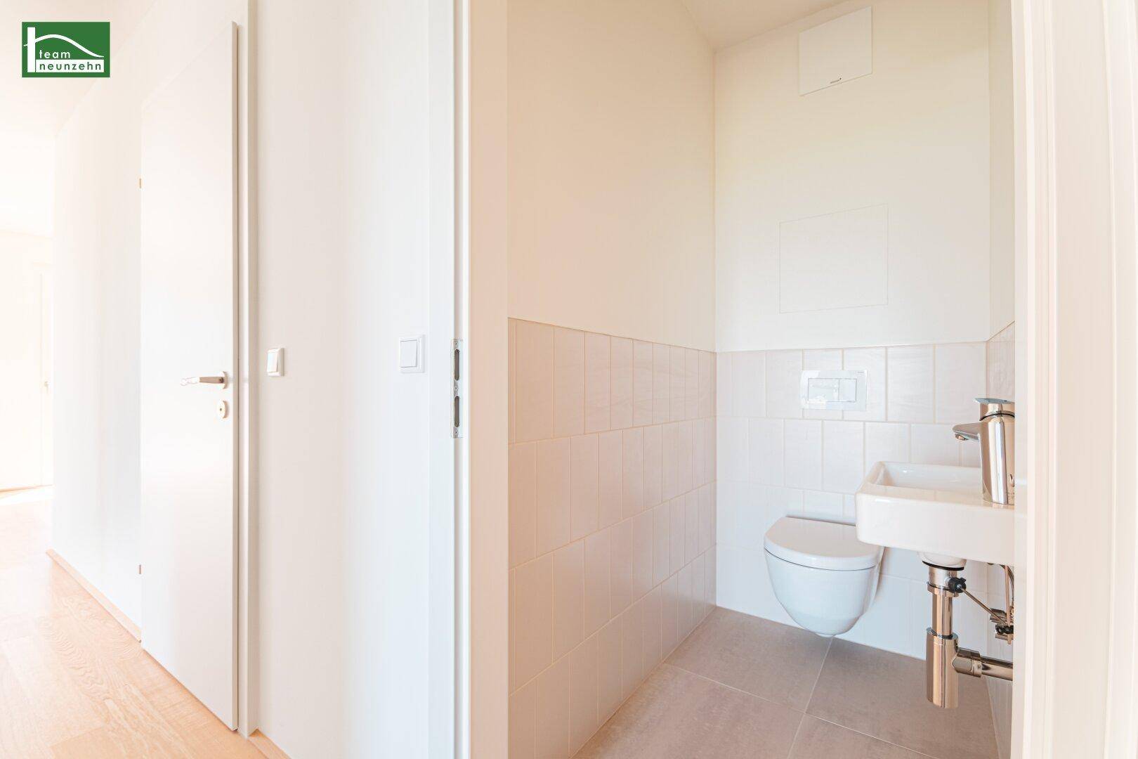 Separate Gästetoilette mit wandhängendem WC und kleinem Waschbecken, hell gefliest.