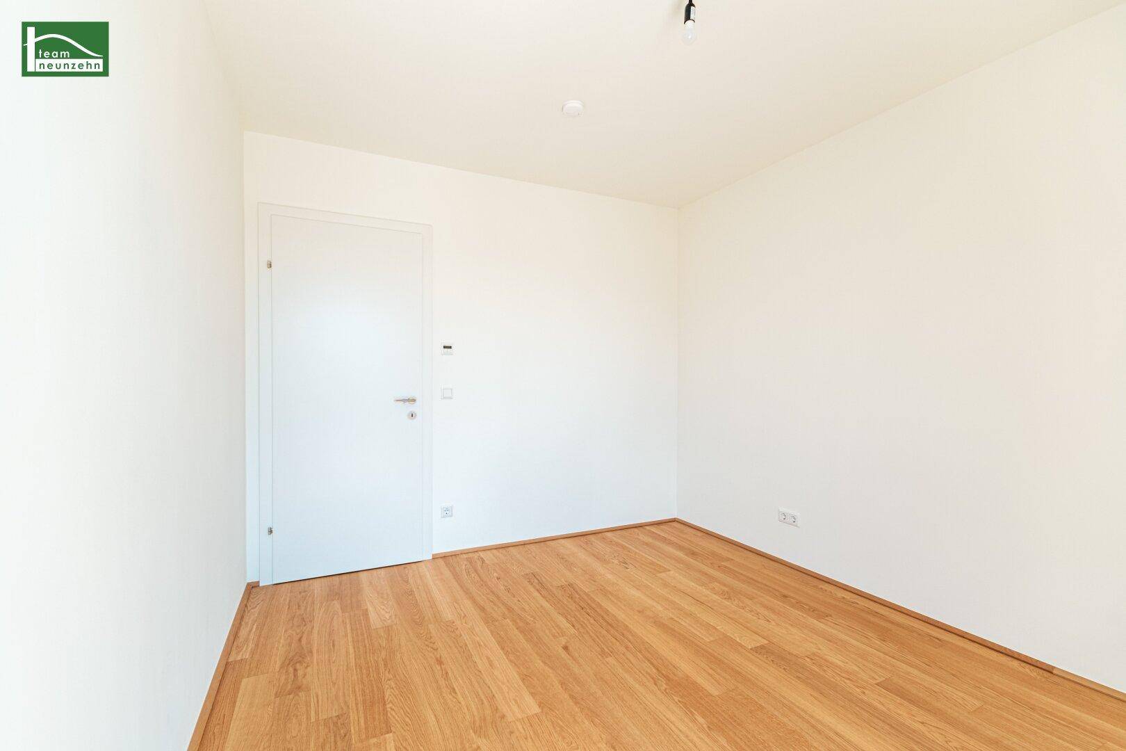 Unmöbliertes Zimmer mit hellem Holzboden und weißer Tür, bereit für die individuelle Gestaltung.