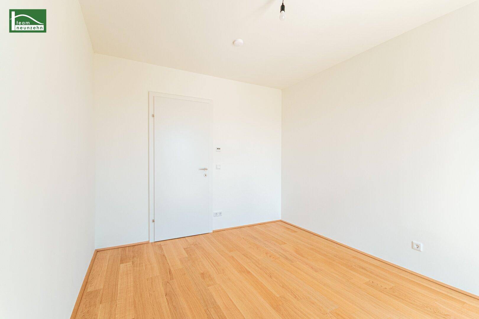 Unmöbliertes Zimmer mit Holzboden und weißer Tür, ideal für ein Schlaf- oder Arbeitszimmer.