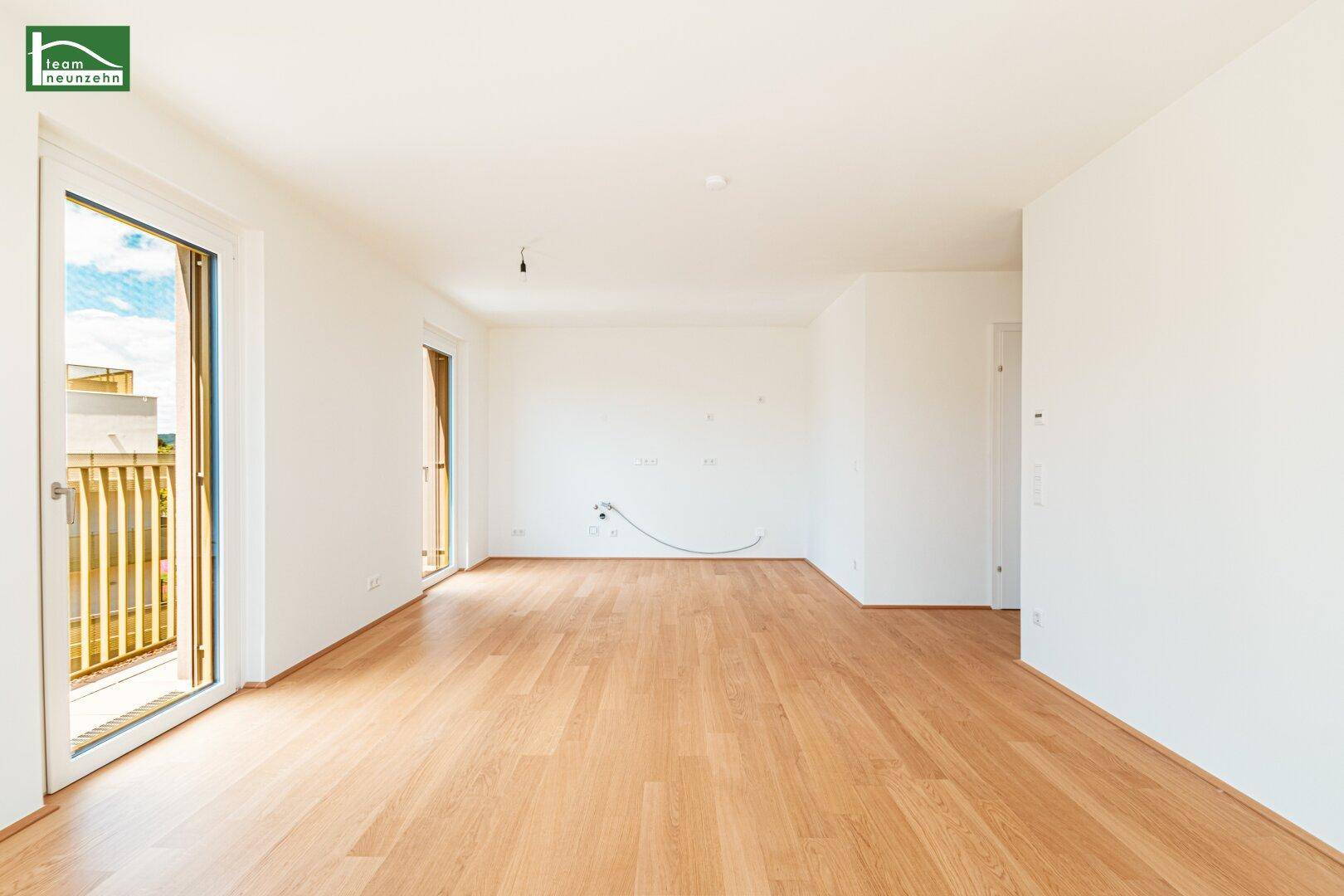 Geräumiges, unmöbliertes Wohnzimmer mit Holzboden und Zugang zu einem Balkon.