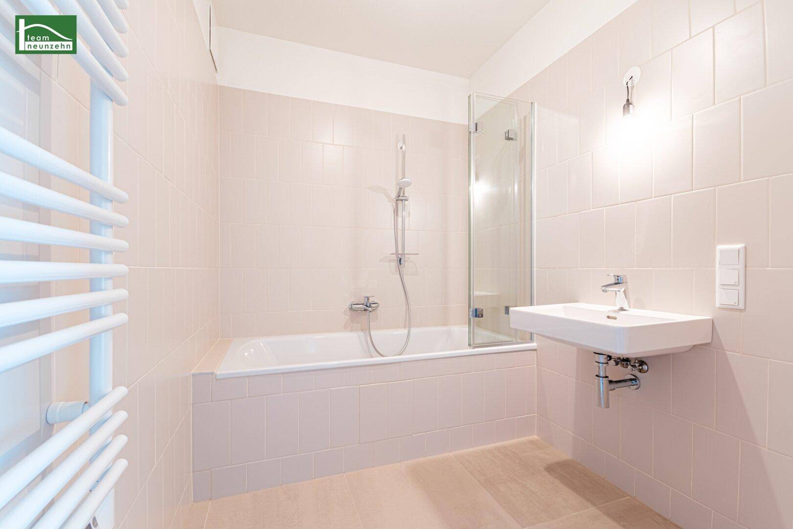 Modernes Badezimmer mit Badewanne, Duschabtrennung und beheiztem Handtuchhalter in hellen Fliesen.
