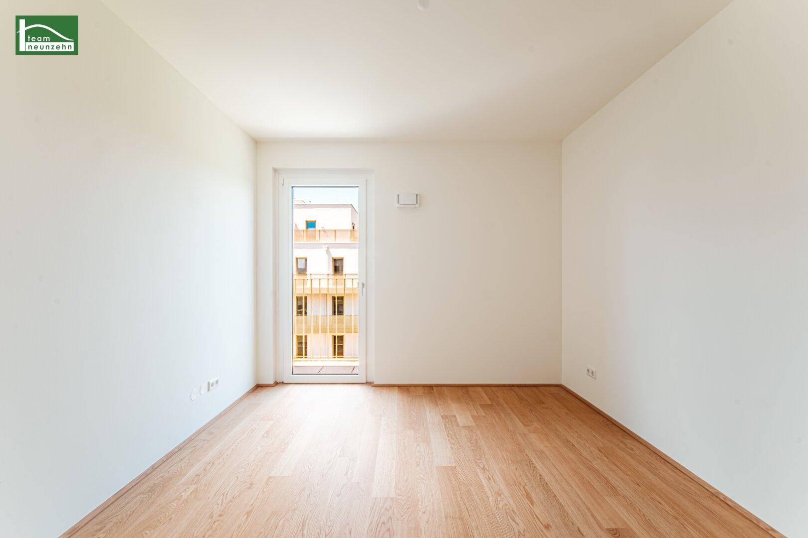 Lichtdurchfluteter Raum mit Holzboden und Zugang zu einem Balkon, ideal für ein Schlaf- oder Wohnzimmer.