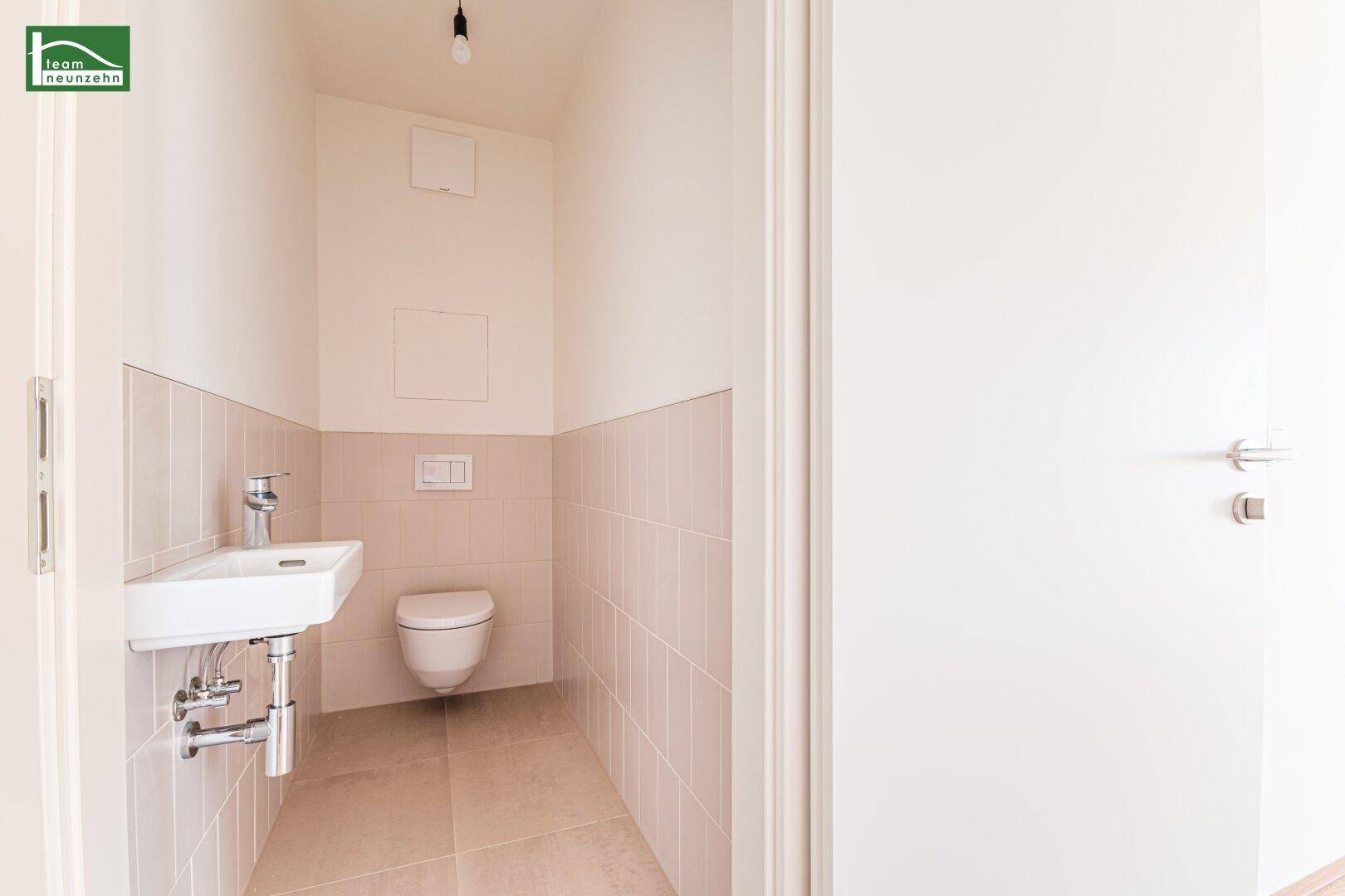 Separates Gäste-WC mit wandhängendem WC und kleinem Waschbecken in neutralen Fliesenfarben.