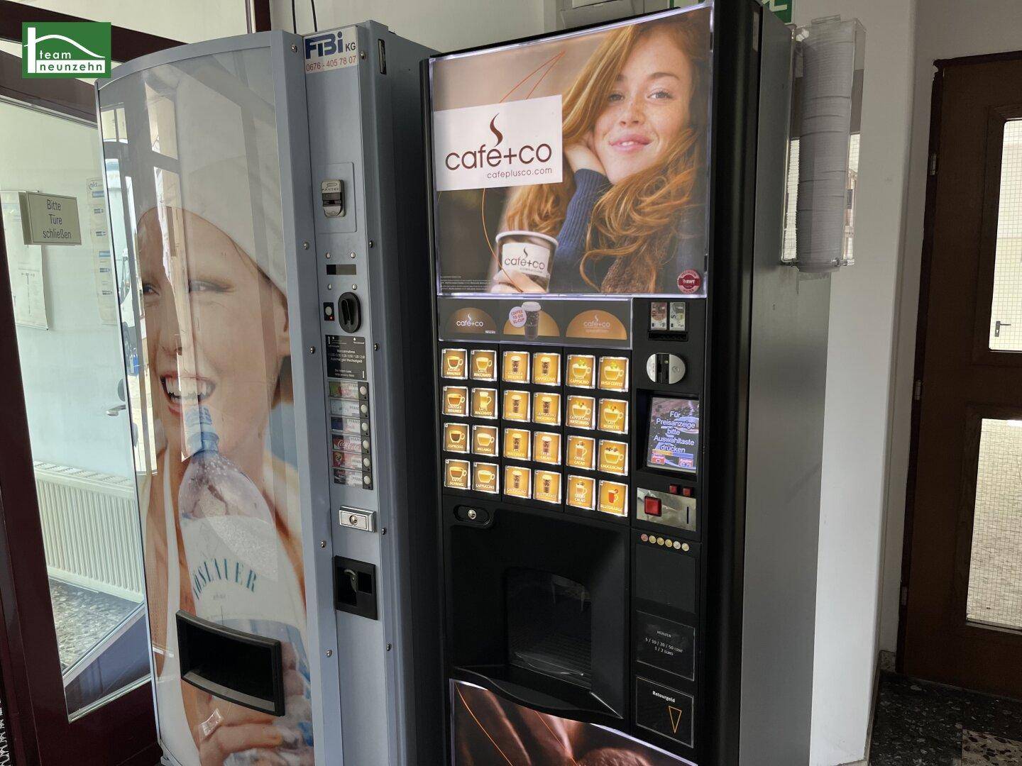 Zwei Verkaufsautomaten, darunter ein Kaffeeautomat, stehen im Eingangsbereich des Gebäudes.